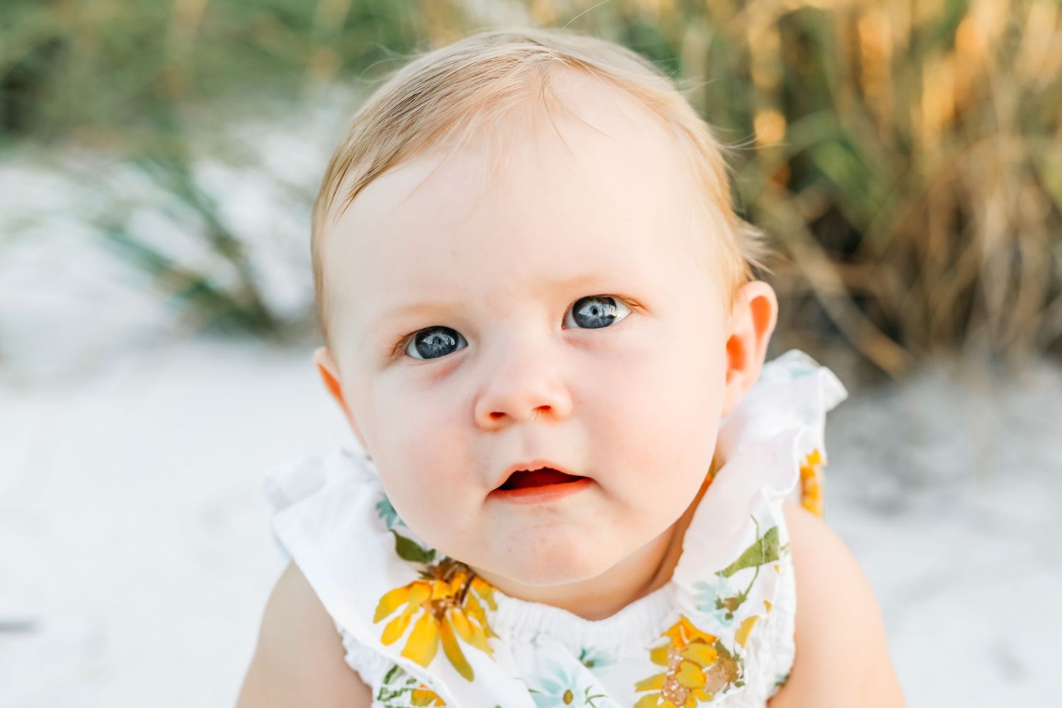 A young child in a white and yellow floral dress smiles sweetly while looking at the camera.