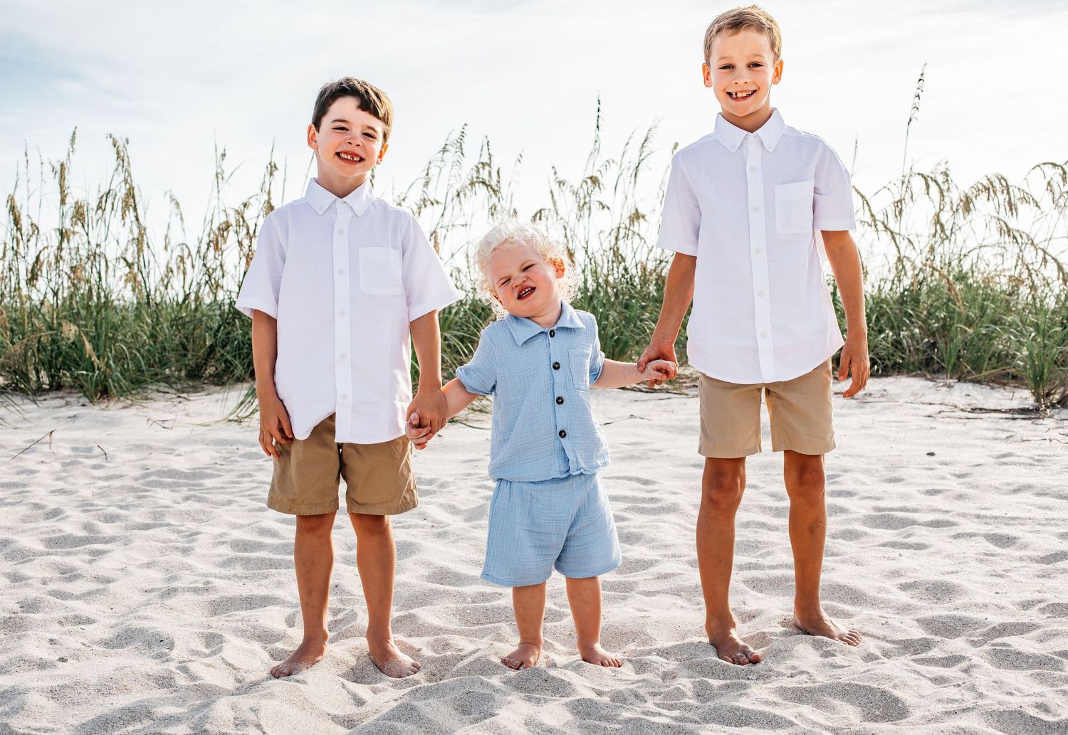 Children's feet lined up on beach sand wearing coordinated white and blue outfits.