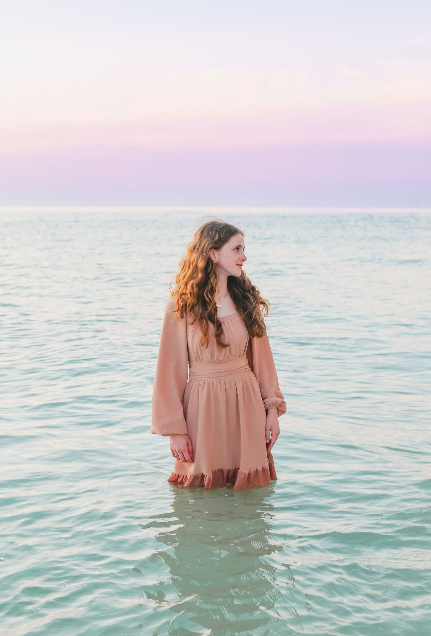 Two young people wading in tranquil turquoise ocean waters at dusk.