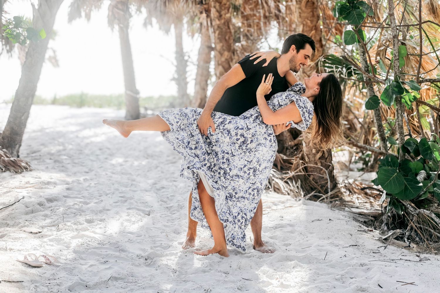 Playful beach photoshoot among palm trees and white sand.