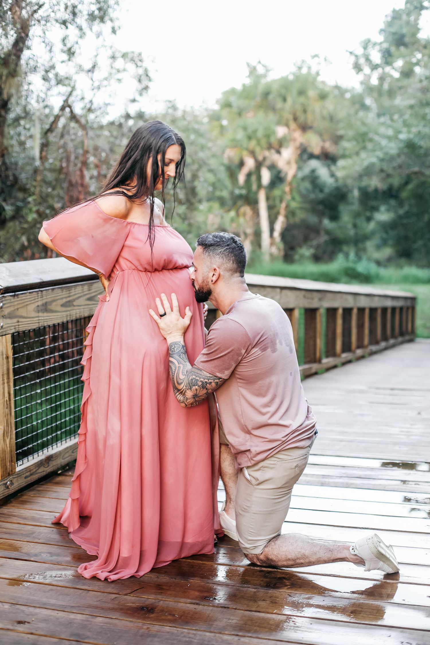 A romantic pregnancy photoshoot on a wooden boardwalk with couple in matching pink and beige outfits.