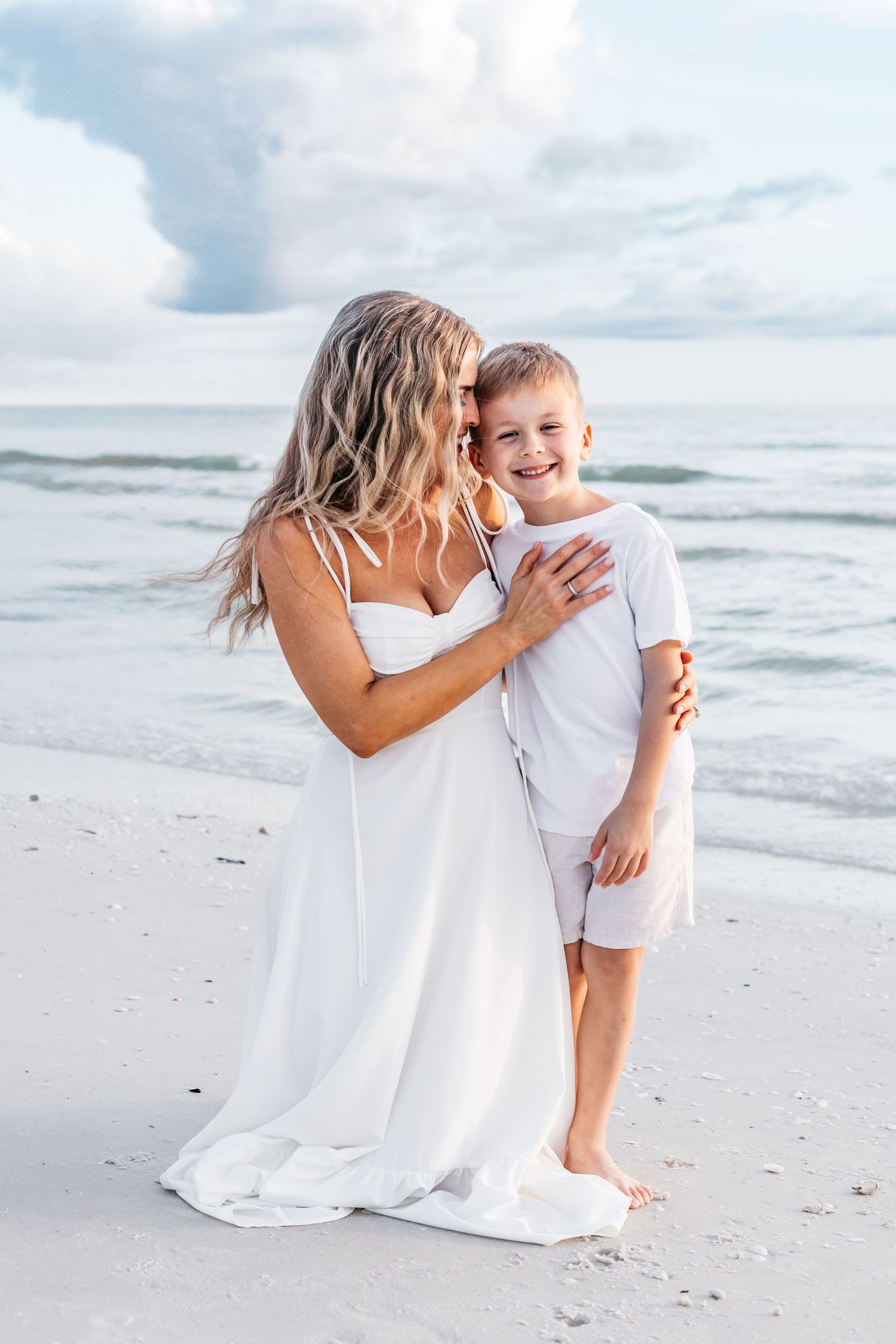 A touching moment between parent and child on a serene white sandy beach with ocean waves in the background.