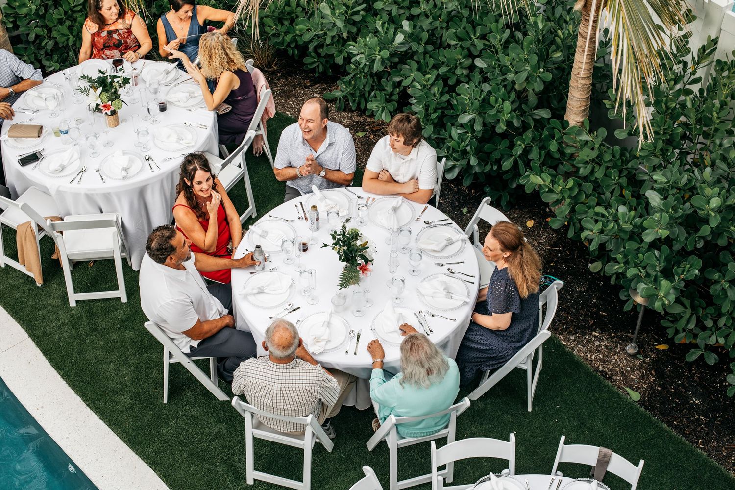 Aerial view of guests seated at round white tables during an outdoor wedding reception on a green lawn.