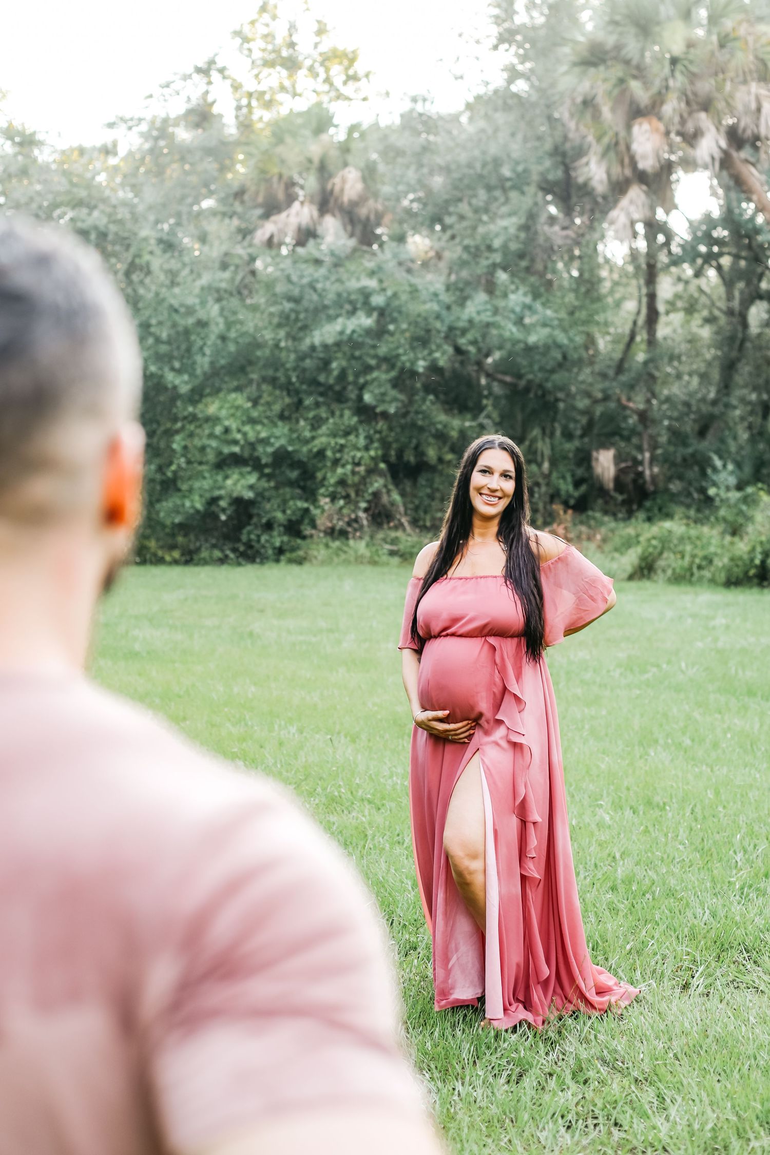 A series of outdoor maternity photos showing a woman in a flowing pink dress posing in a grassy field at sunset.