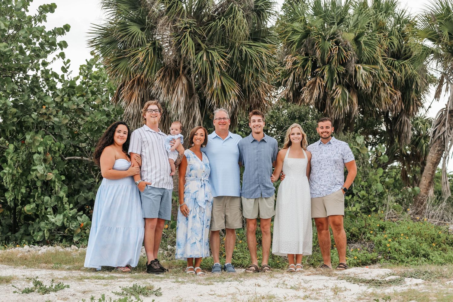 A happy family of seven poses together outdoors near palm trees at a Florida beach.