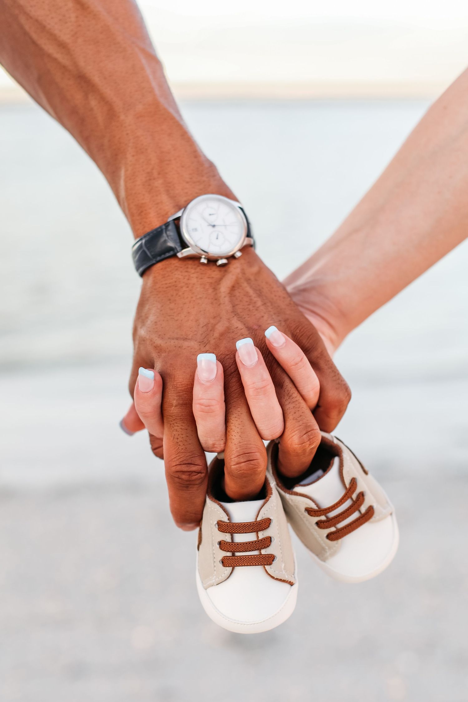Hands holding small white baby shoes with brown laces against a bright background.