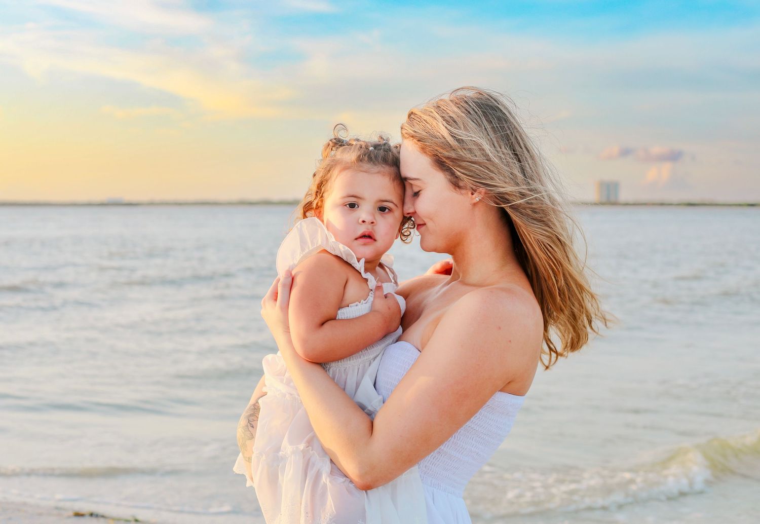 Mother and child share tender moment on beach at sunset.