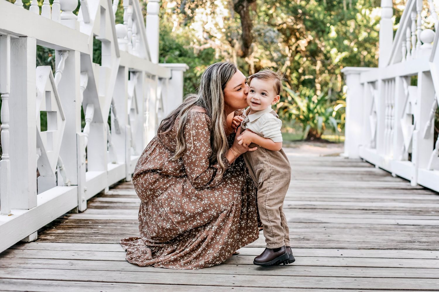 A romantic couple shares tender moments on a white wooden bridge surrounded by lush greenery.