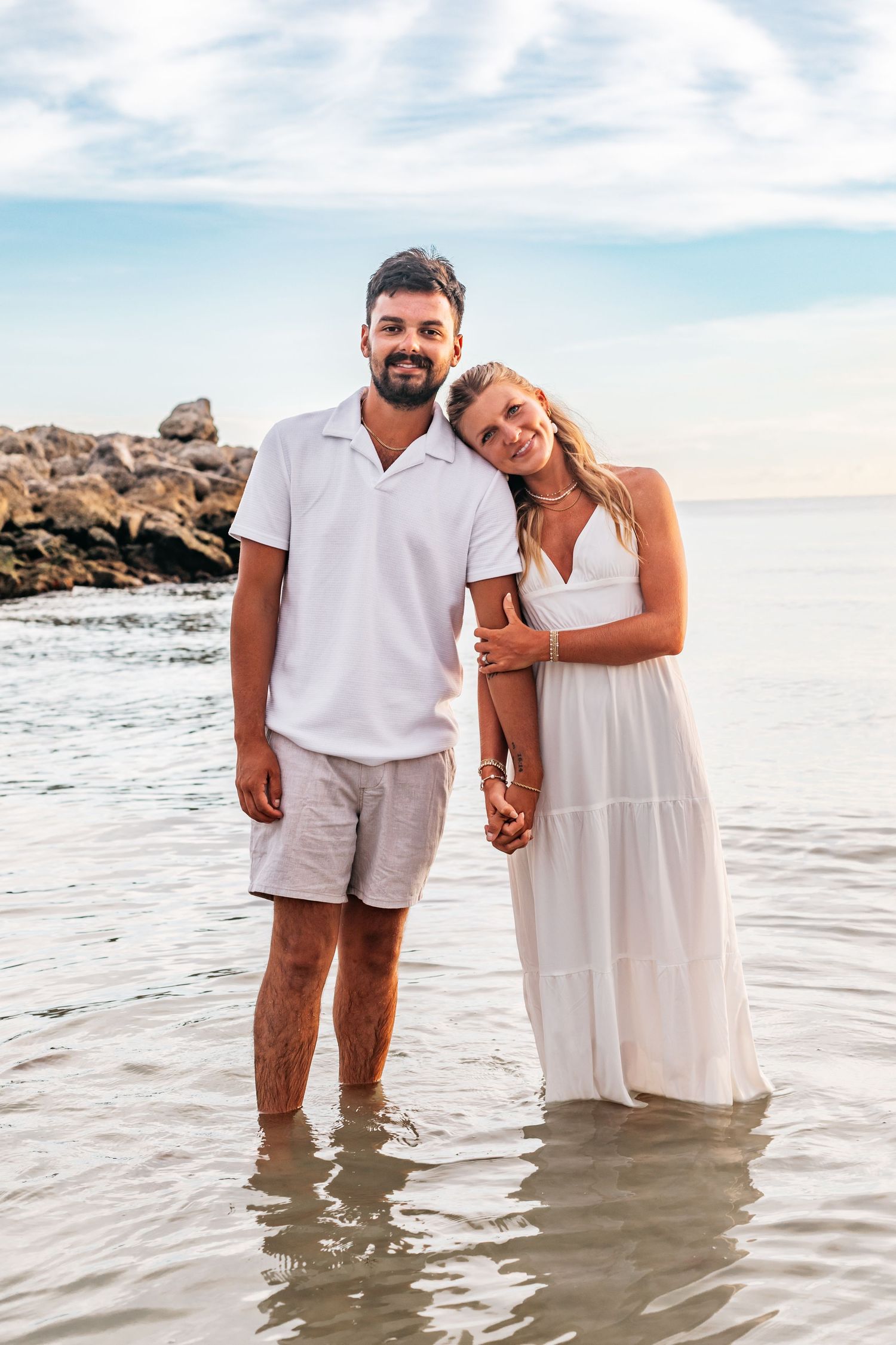 Couple stands in shallow ocean water during beach photoshoot.