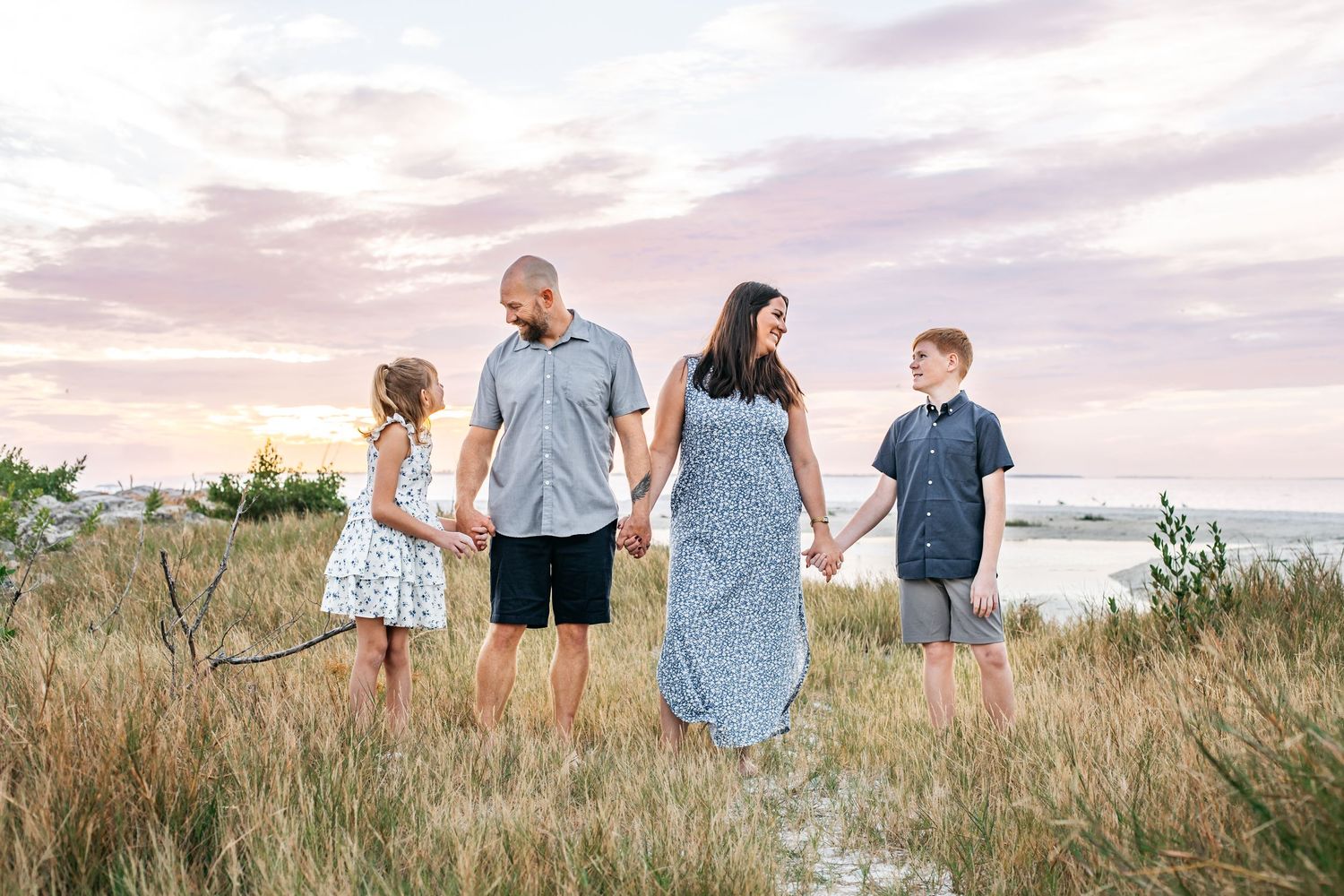 A group walks together through tall grass and wildflowers along a coastal path during golden hour.