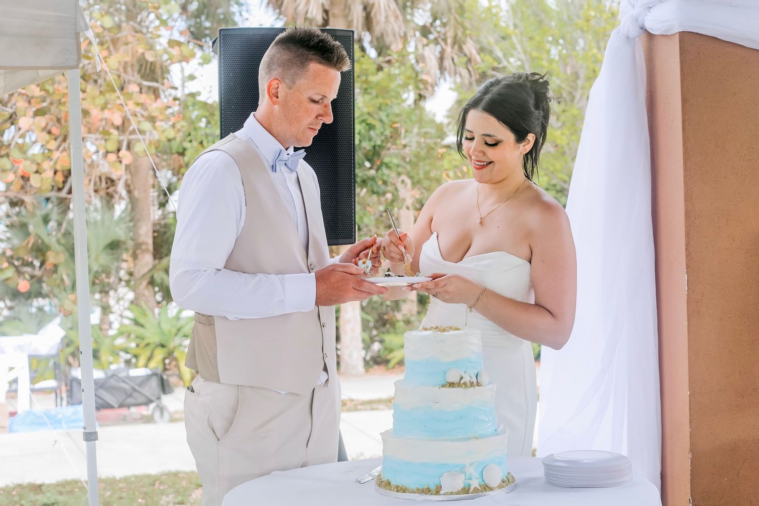 Bride and groom cutting a blue wedding cake outdoors at a garden reception ceremony.