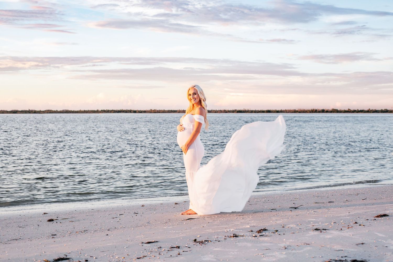 A person in a flowing white dress walks along a tranquil beach at sunset creating a dreamy silhouette.