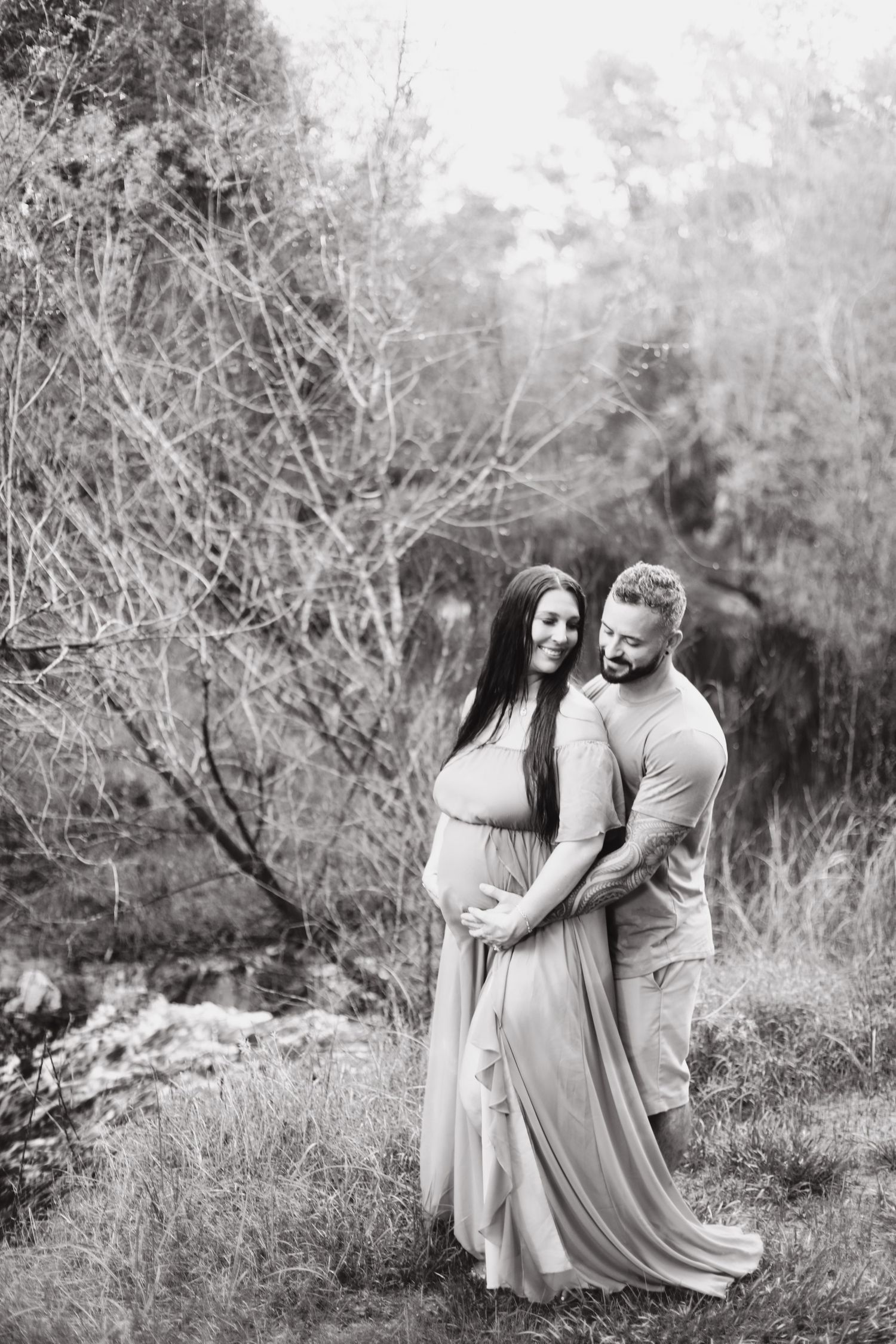 A couple in light flowy dresses share tender moments together in a natural outdoor setting across multiple black and white photos.