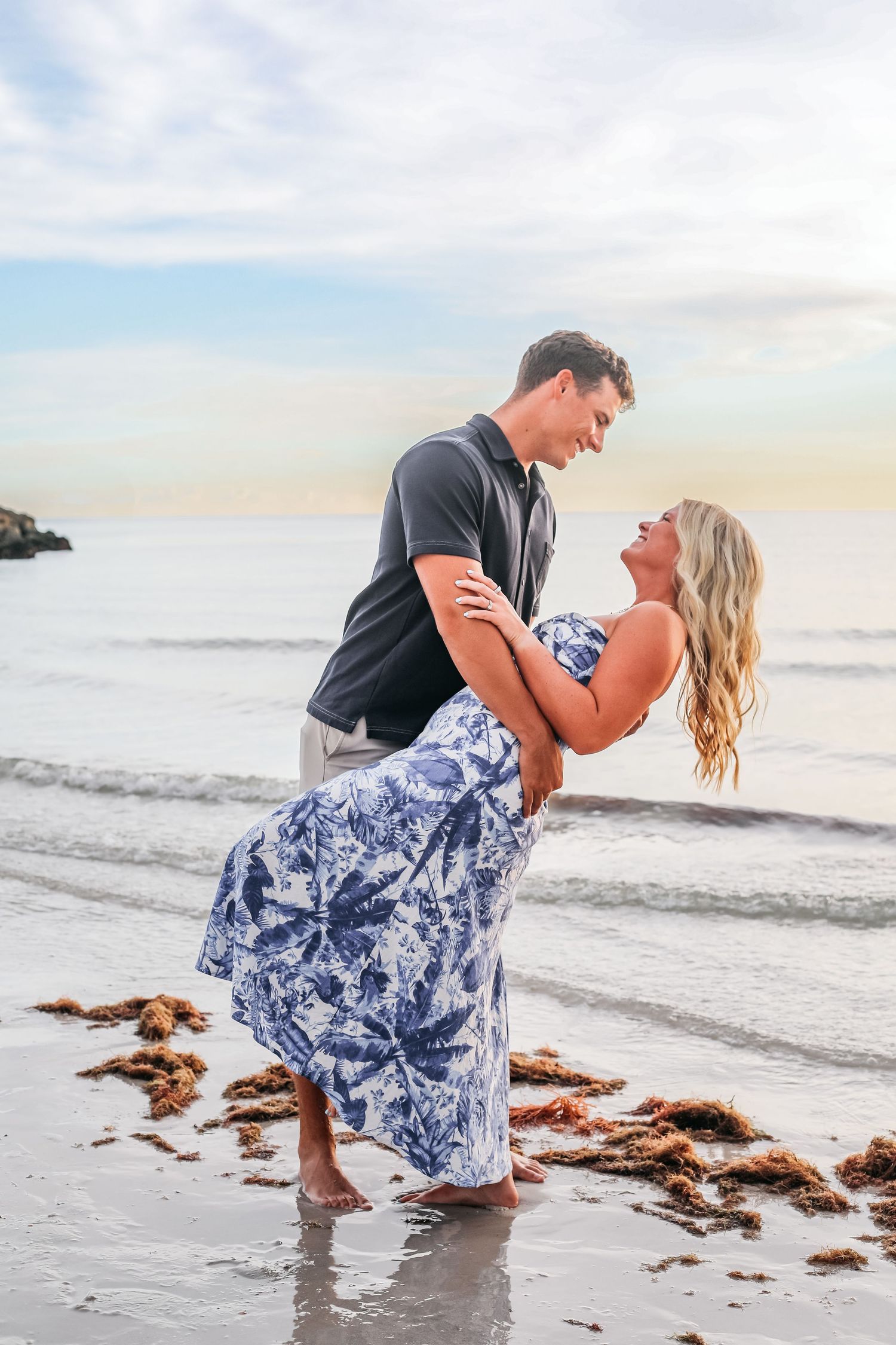 Couple in coordinated outfits dancing and dipping on beach at sunset.