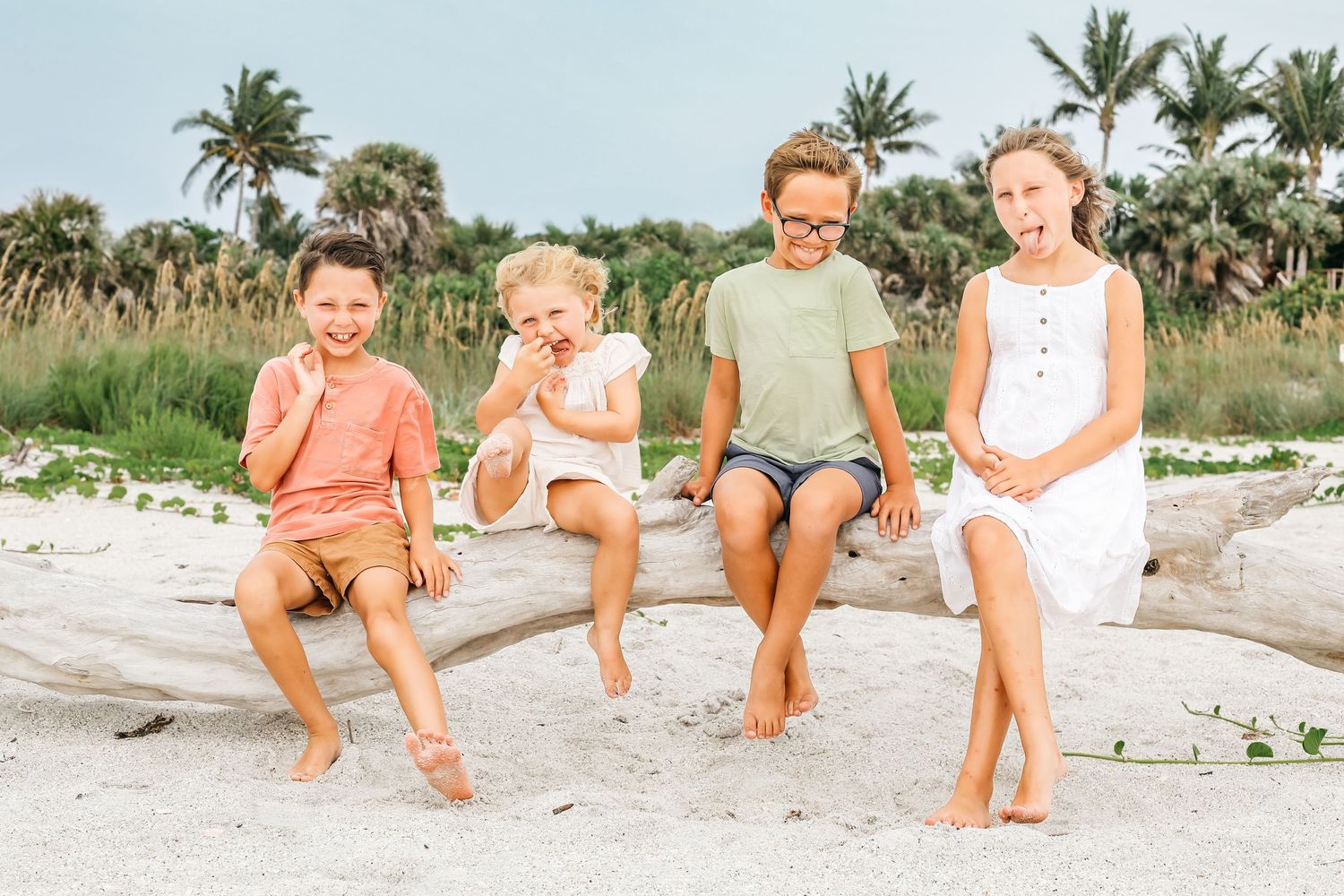 A group relaxes together on a sandy beach wearing coordinated pastel and neutral colored outfits.