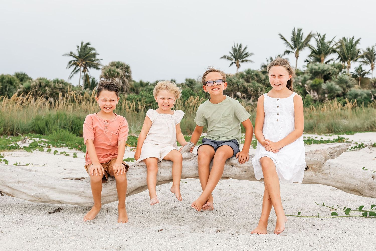 Family enjoying a sunny day sitting together on the sandy beach with palm trees in the background.