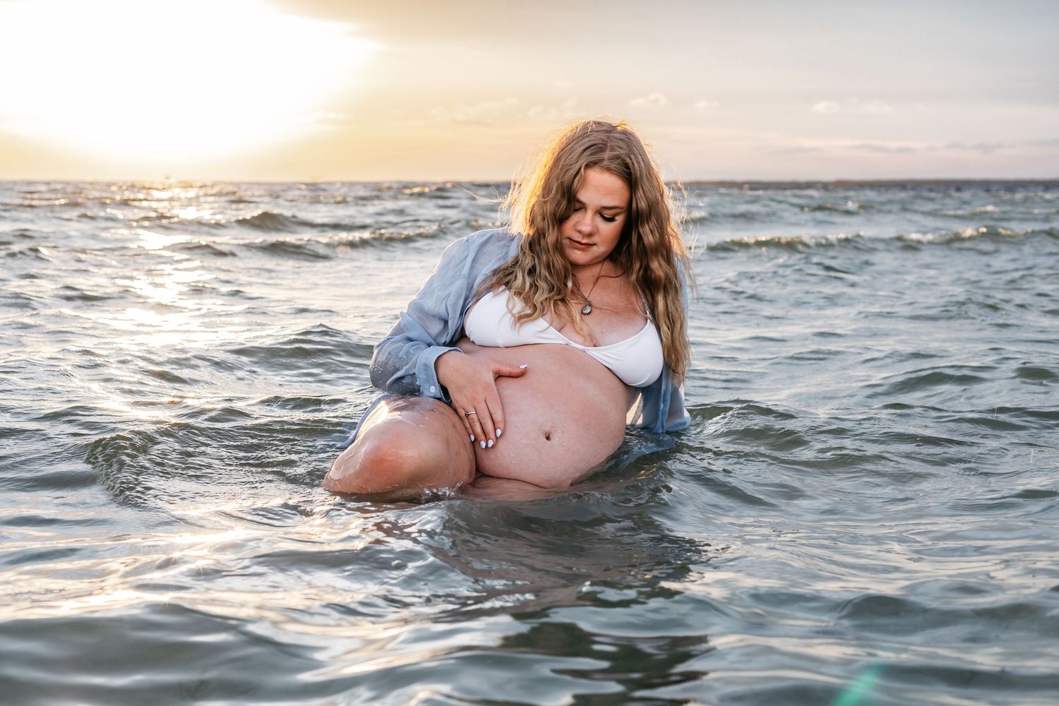 Woman in swimwear poses in ocean water during golden hour photoshoot.
