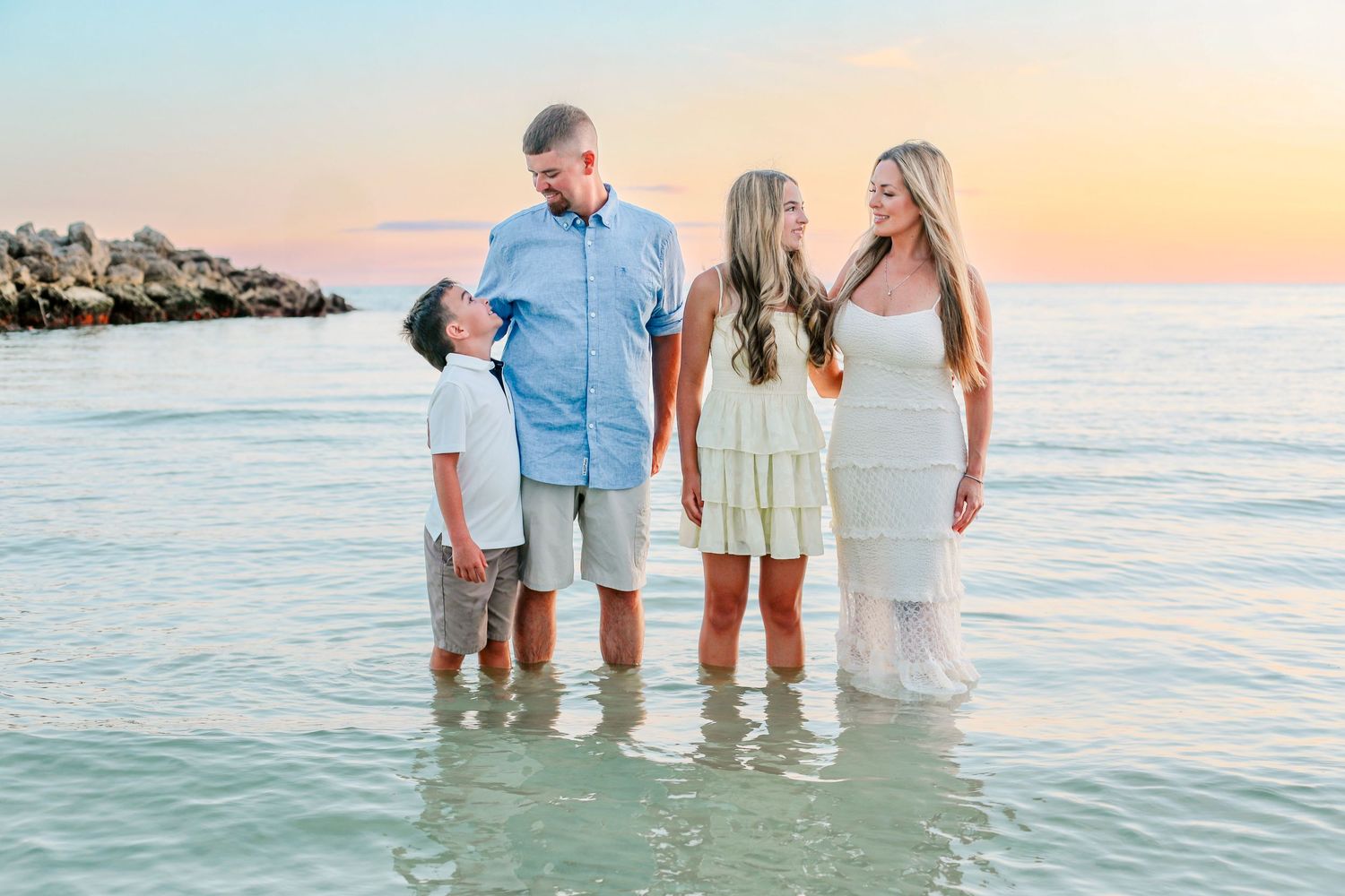 Family dressed in white and light colors standing together at a beach during sunset.