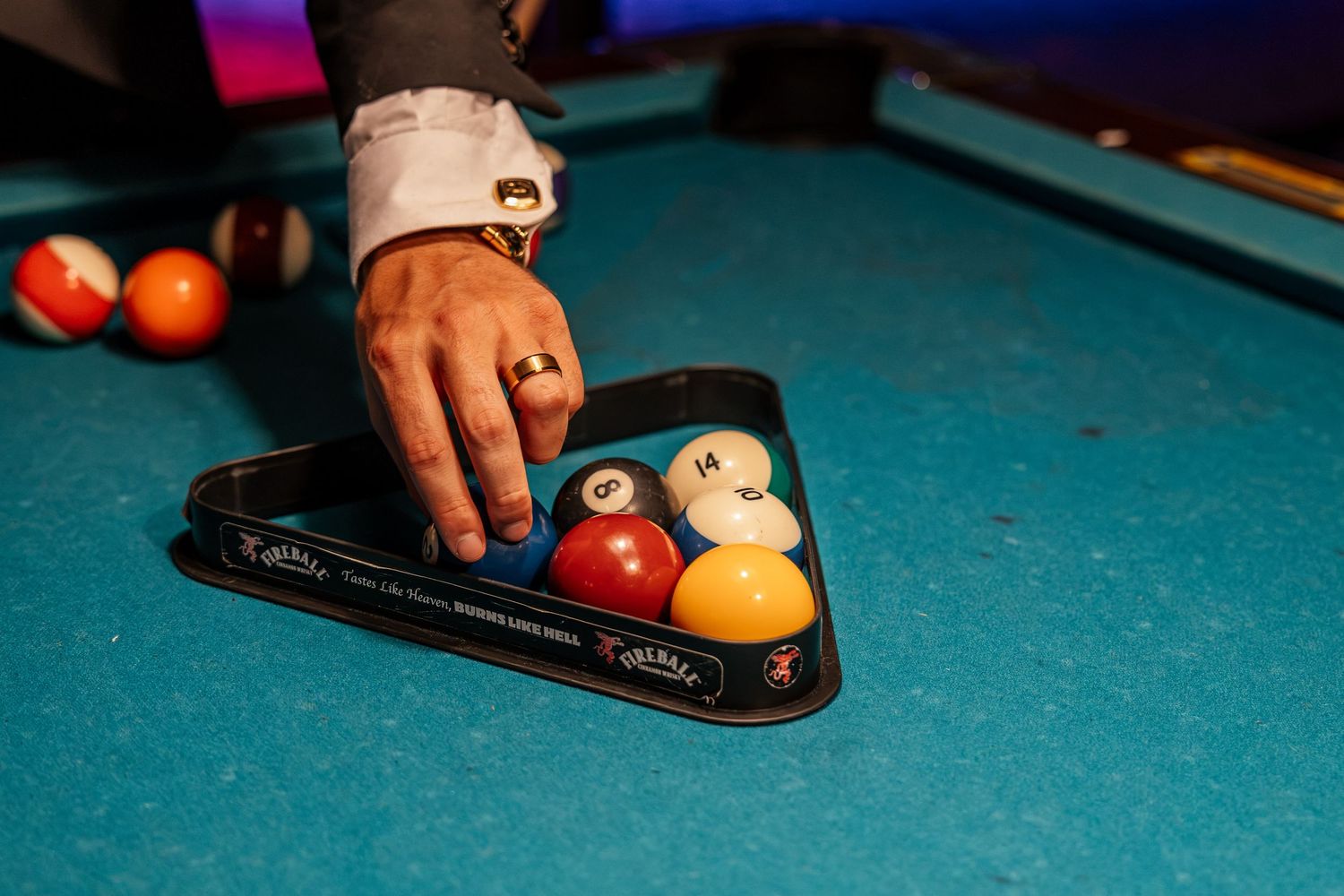 Person arranging colorful billiard balls in a triangle rack on a blue pool table.