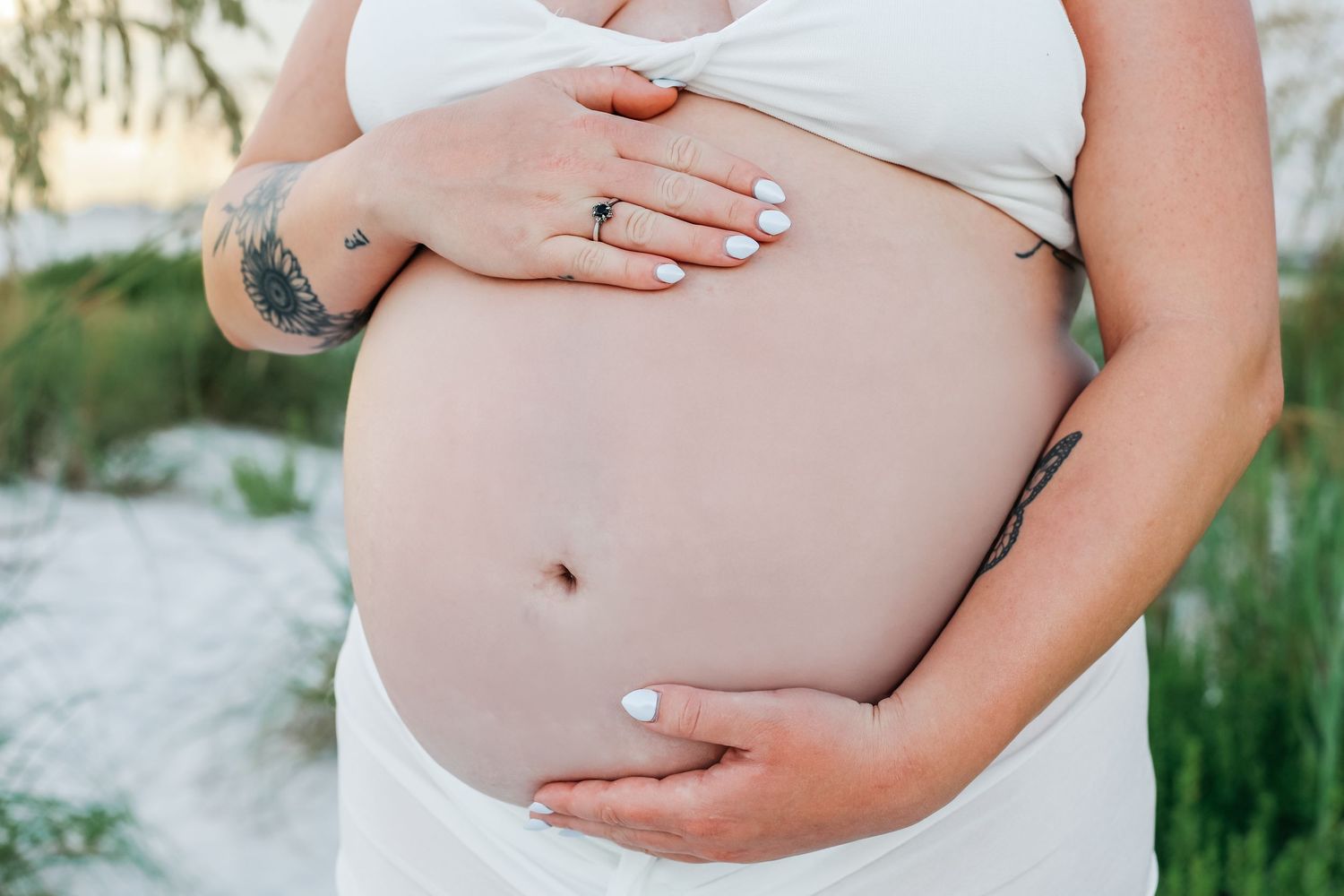 Close-up view of hands gently cradling a pregnant belly against white fabric.