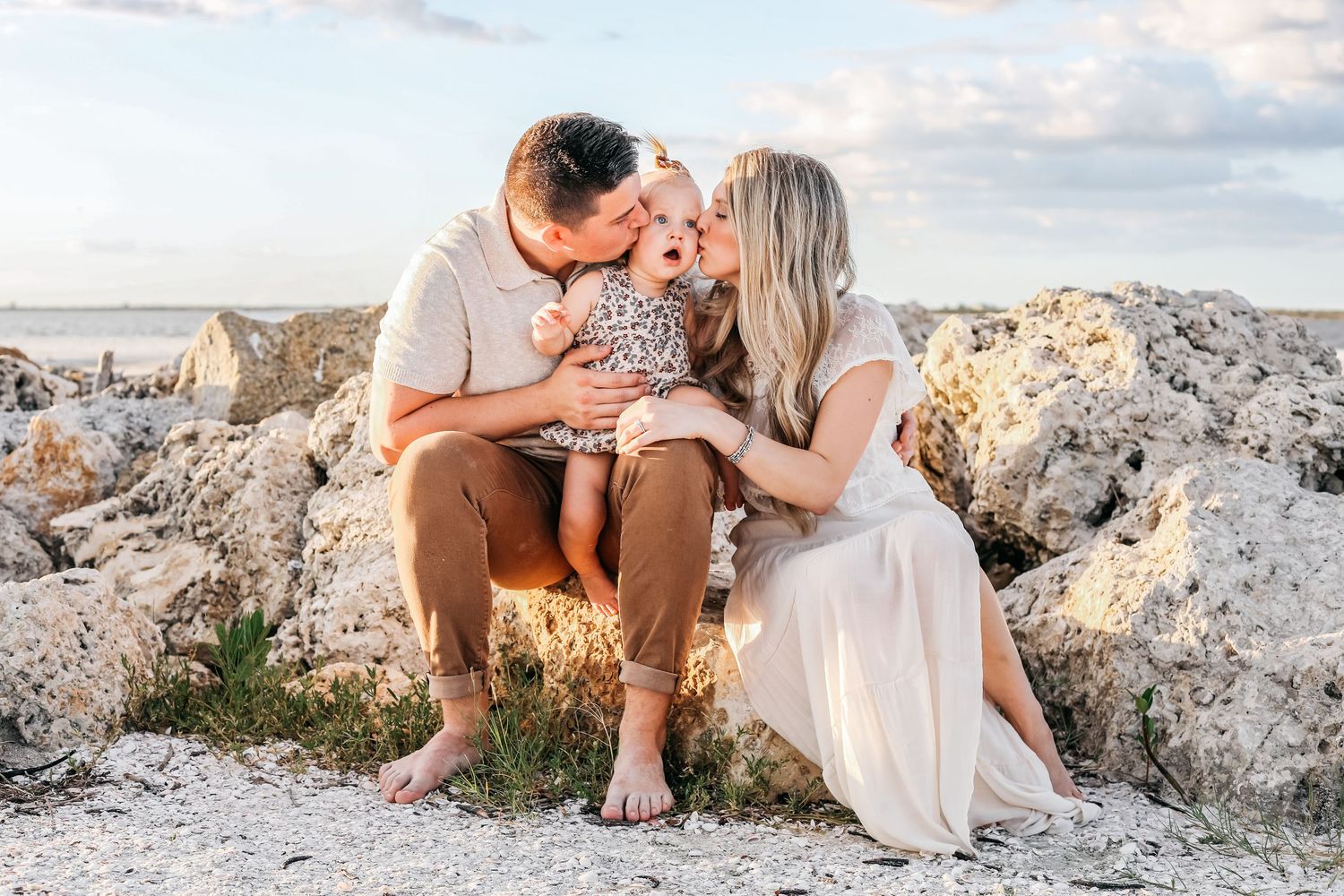 Couple and their dog sit together on rocky coastal terrain during sunset photo session.