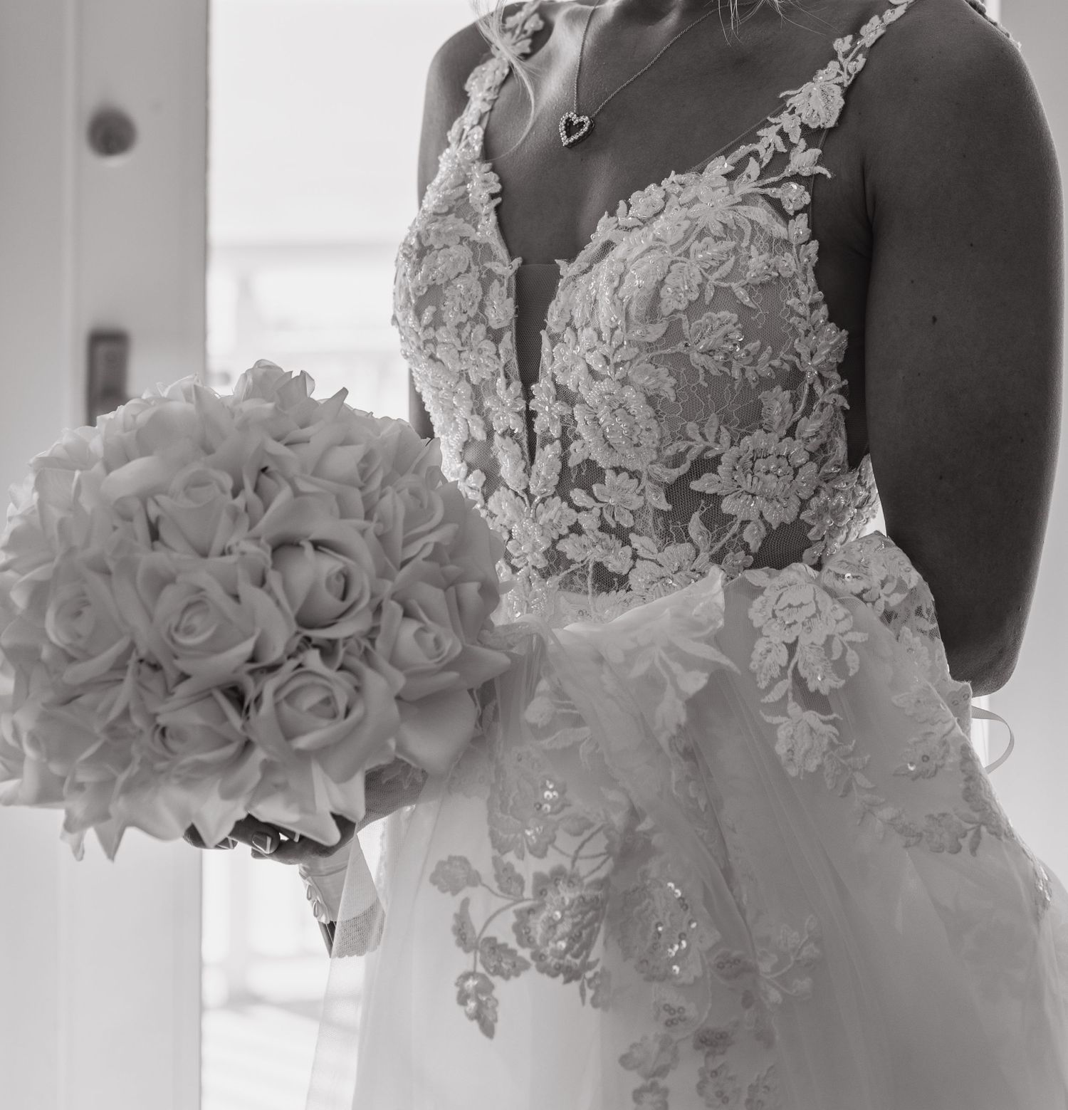 Black and white photo of a bride in lace wedding gown holding a round bouquet of roses.