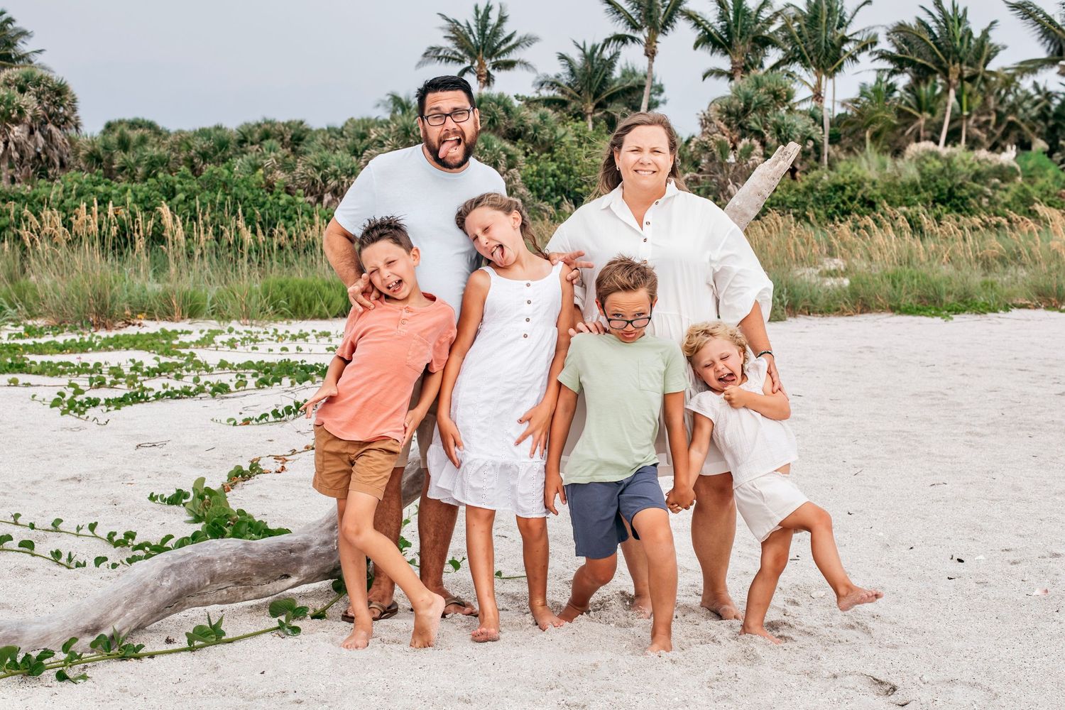 A group of people wearing coordinated brown and white outfits pose together for family photos on a sunny beach.