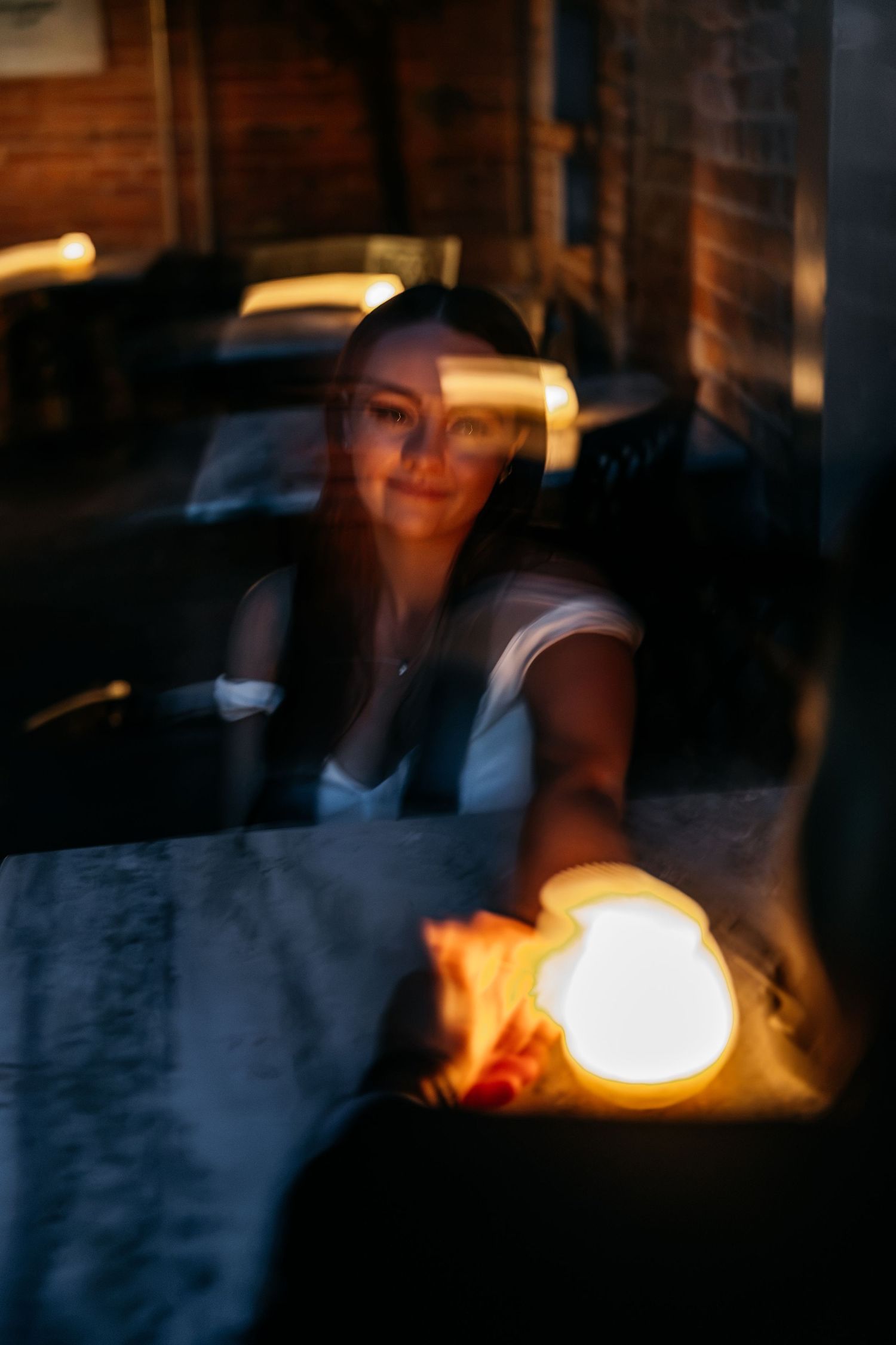 Woman smiling at candlelit restaurant table in warm, moody evening ambiance.