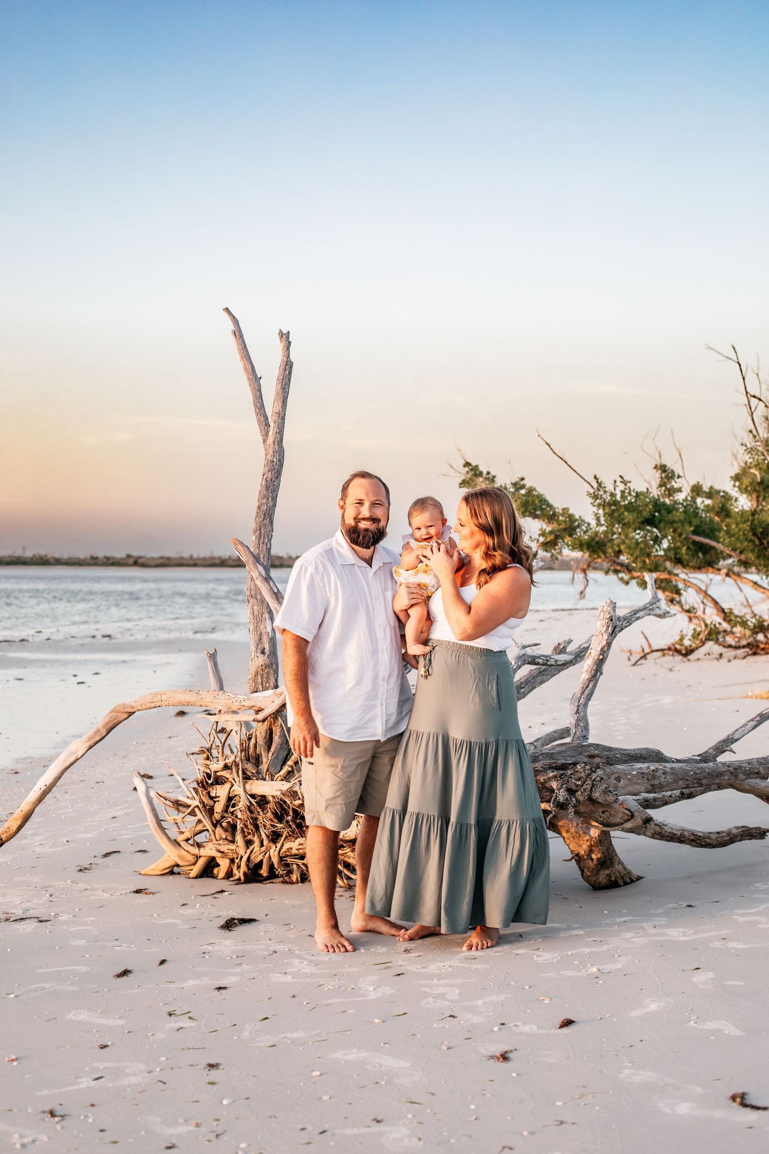 Family beach photos at sunset with driftwood and ocean backdrop.