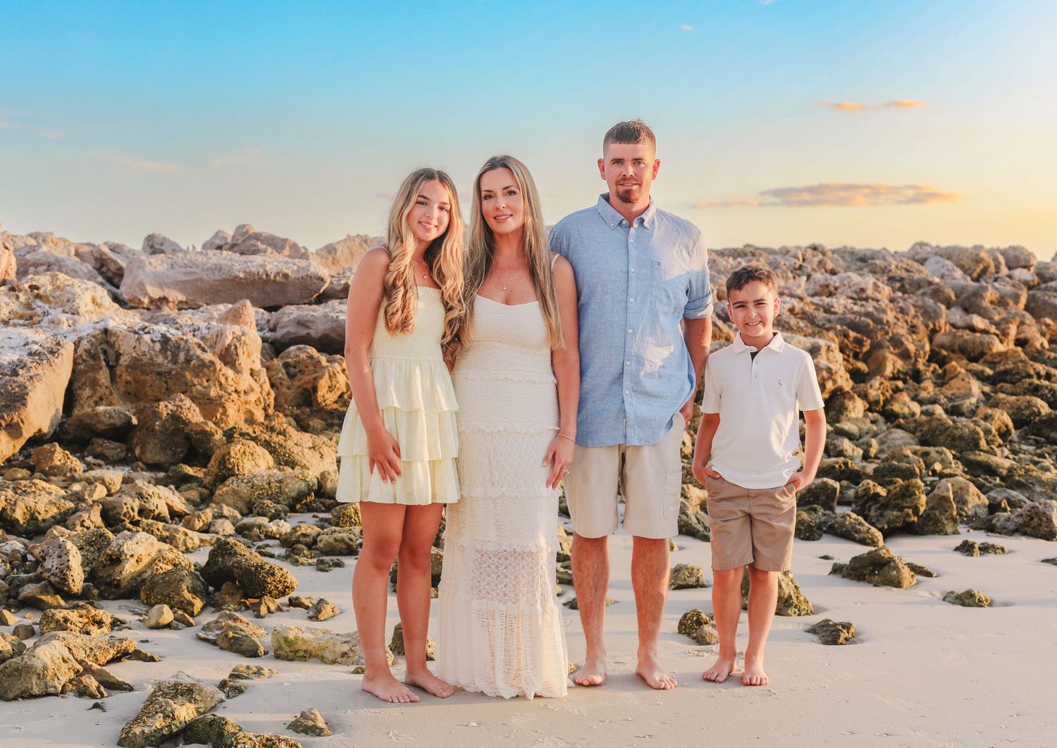 A beach photoshoot with a group wearing coordinated outfits on rocky shore at sunset.