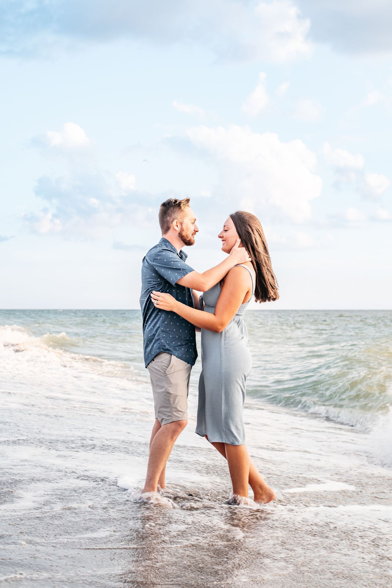 A couple shares a romantic moment while standing in the ocean waves at the beach during a sunny day.