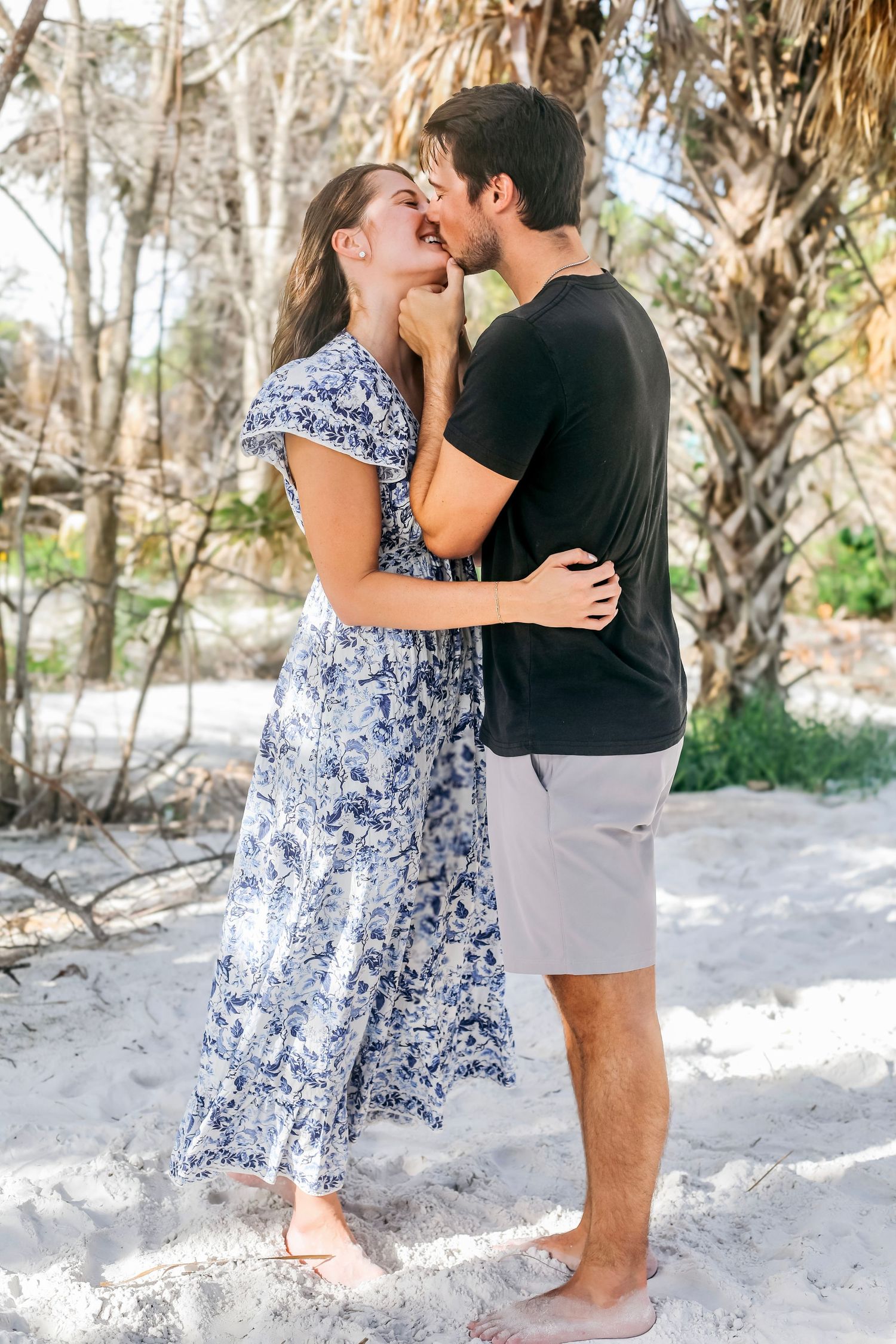 Romantic beach photoshoot with couple embracing among palm trees.