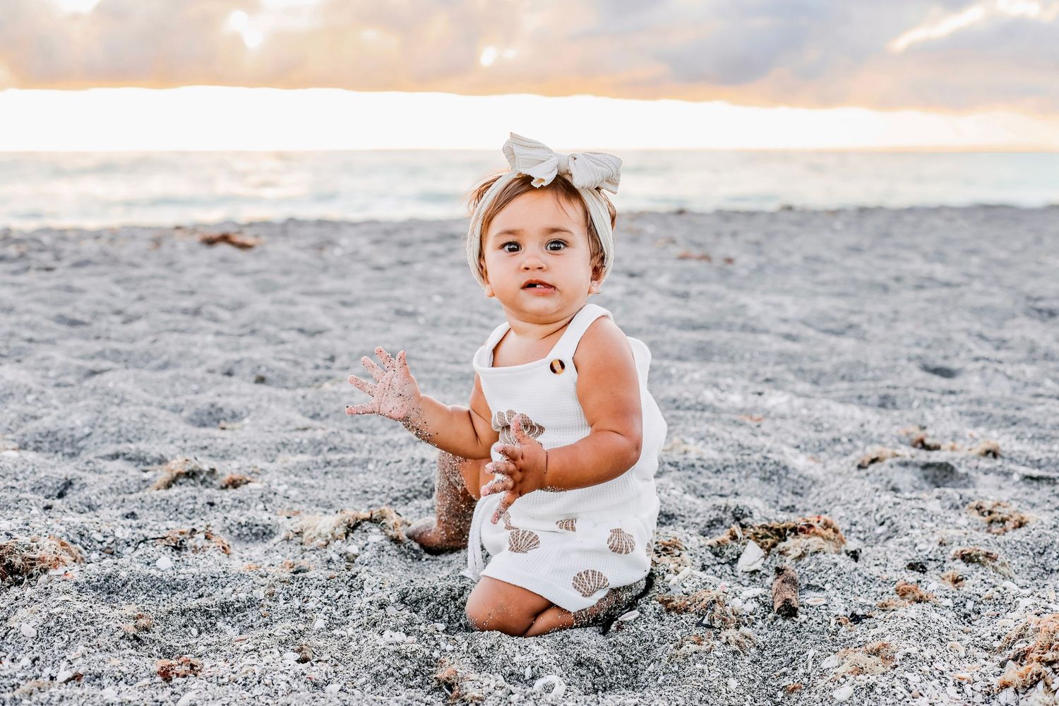 A small child plays on a sandy beach at sunset while wearing a white dress.