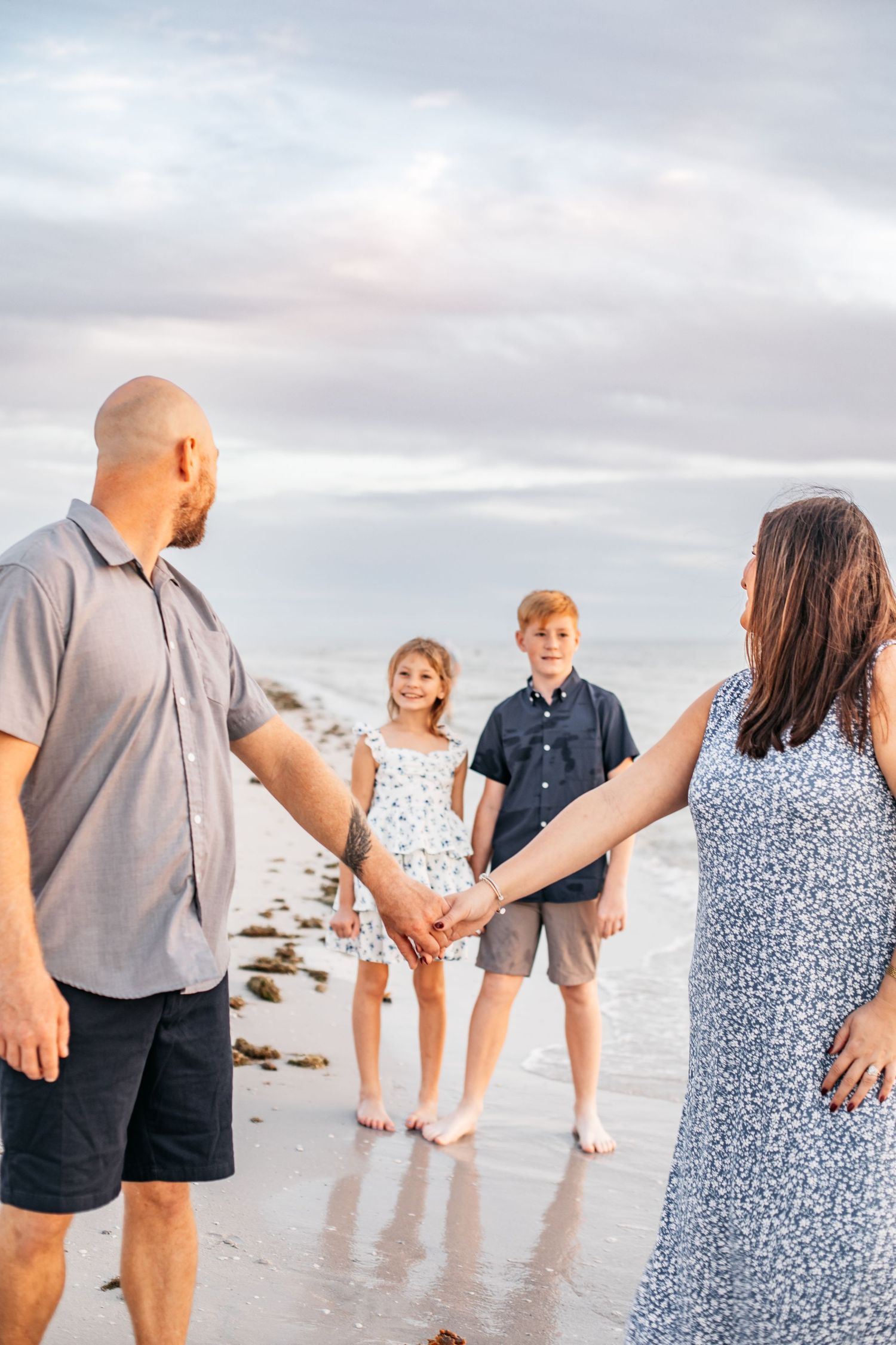 A family holds hands while walking along the shoreline during sunset at the beach.