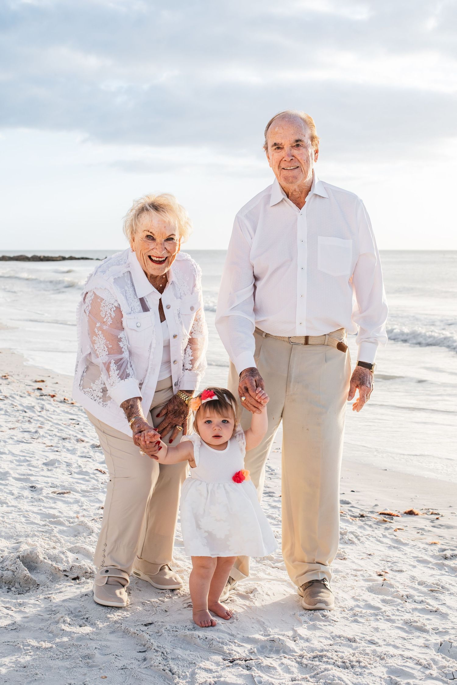 Family enjoying a tender moment together while walking along a white sandy beach at sunset.