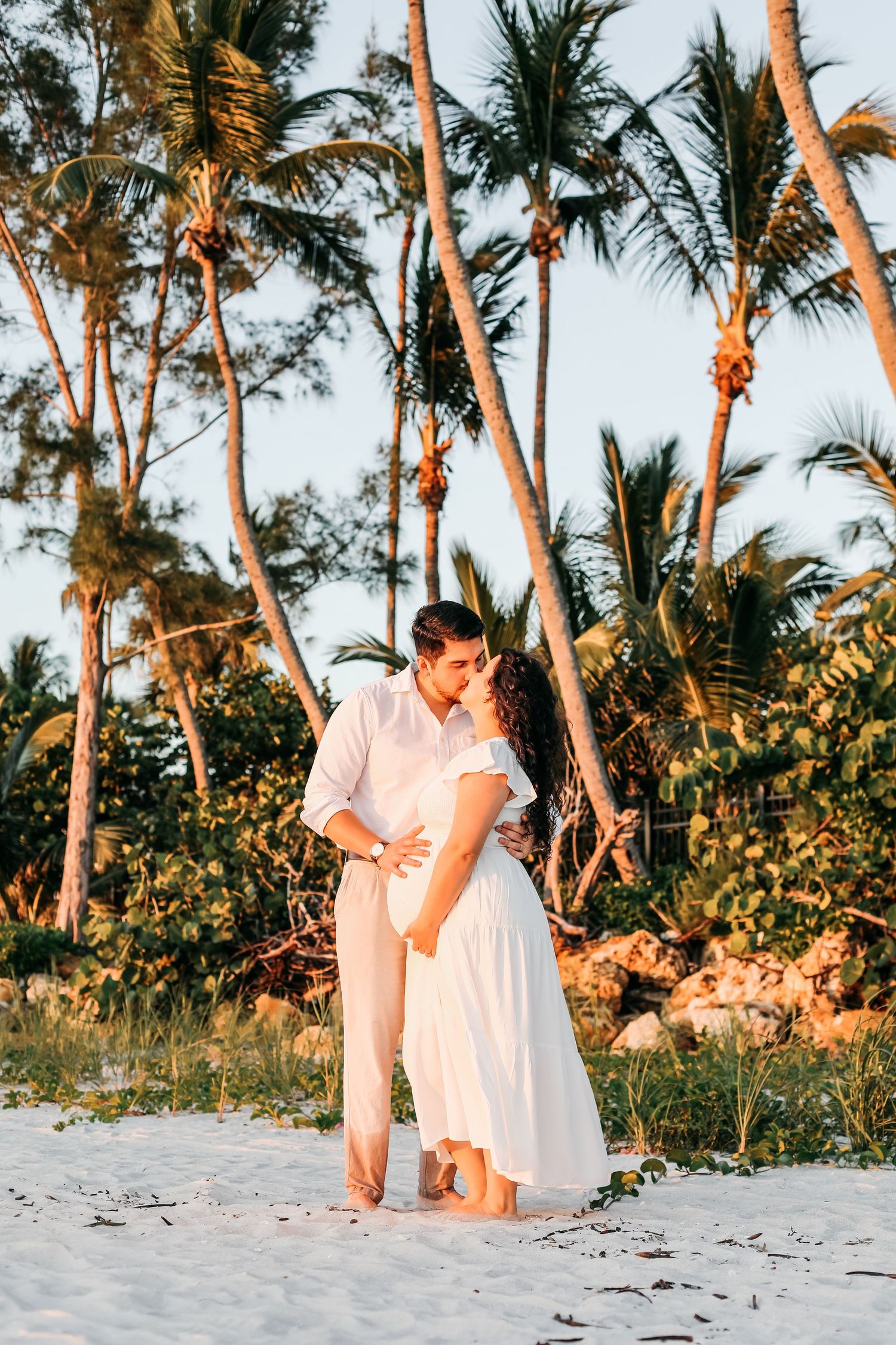 A romantic beach photoshoot at sunset with palm trees and white sand creating a dreamy tropical backdrop.