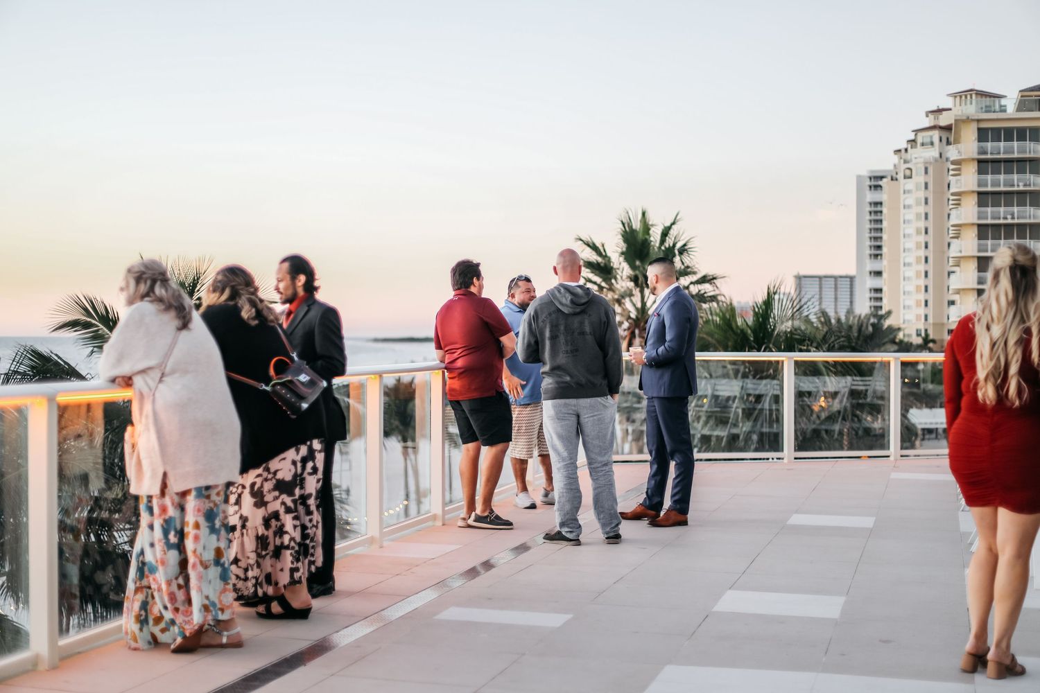 Guests mingle on a rooftop terrace at sunset with ocean and city views in the background.