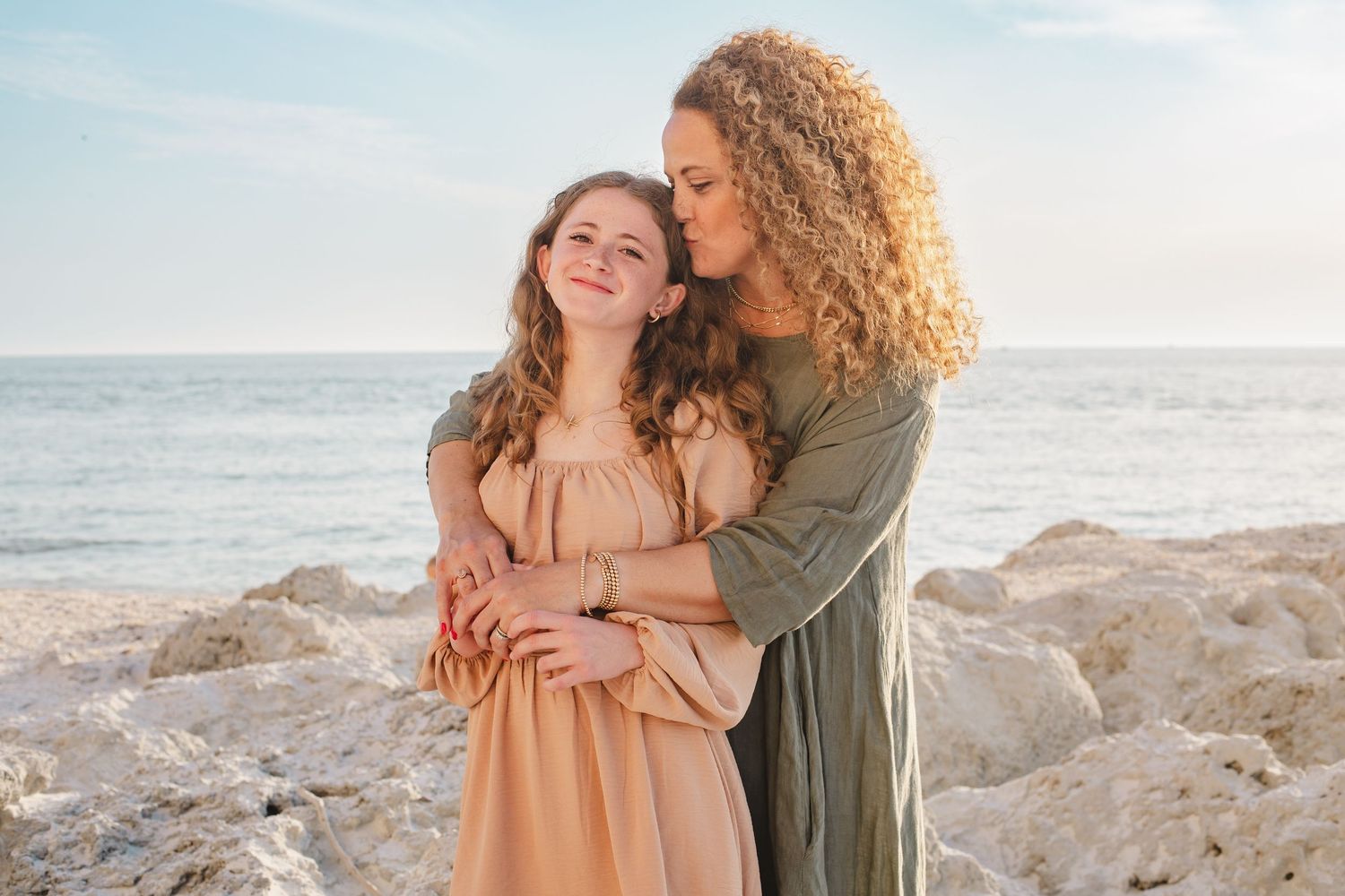 Two people share an intimate embrace on a rocky beach at sunset.