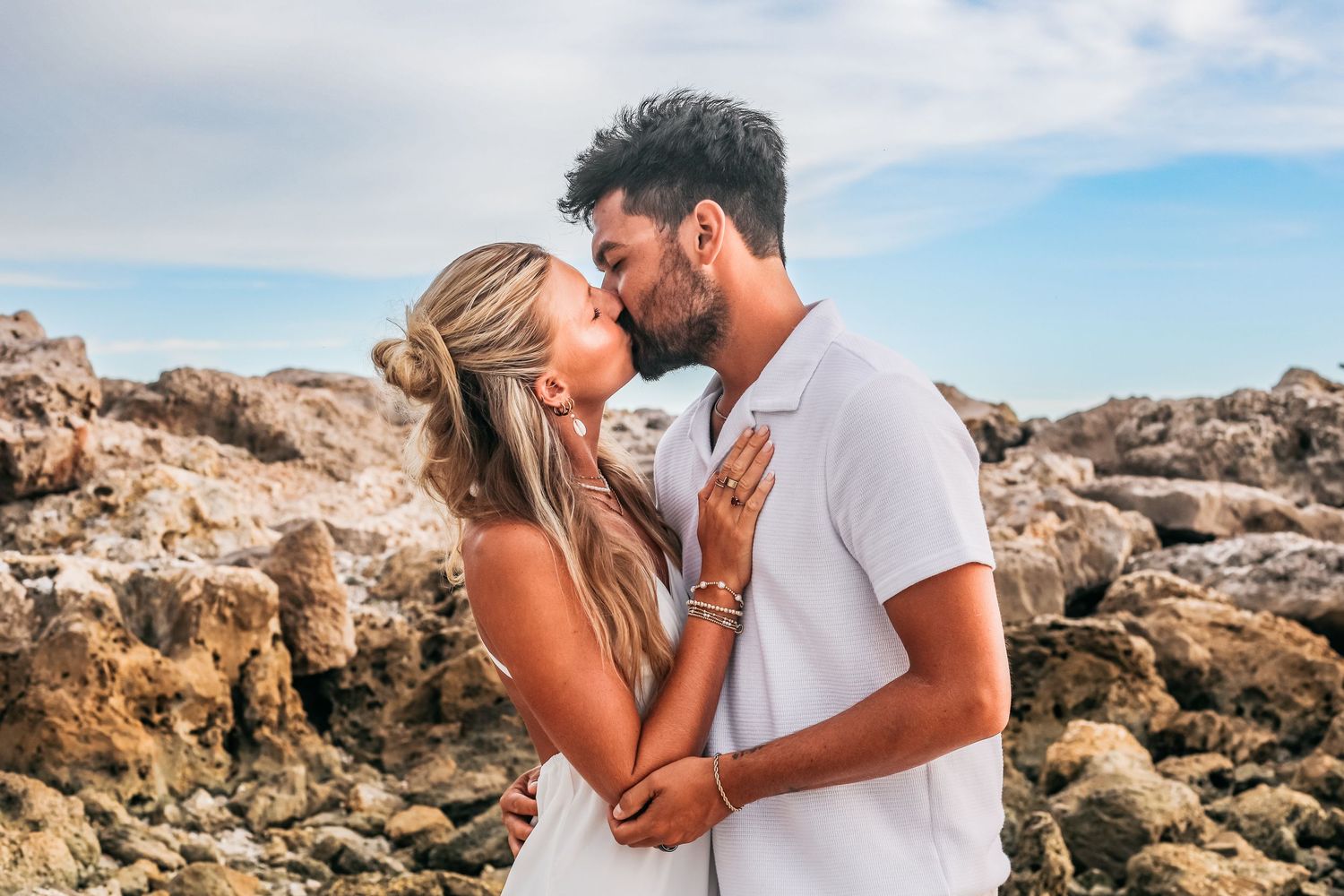 Romantic couple sharing tender moments together on rocky beach at sunset.