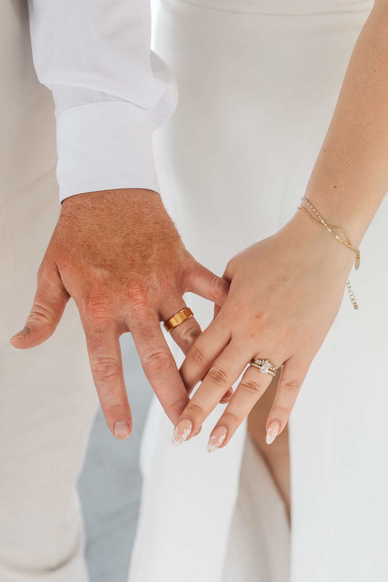 Newlywed couple holding hands displaying wedding rings, bride wearing diamond ring and bracelet, groom with gold band.