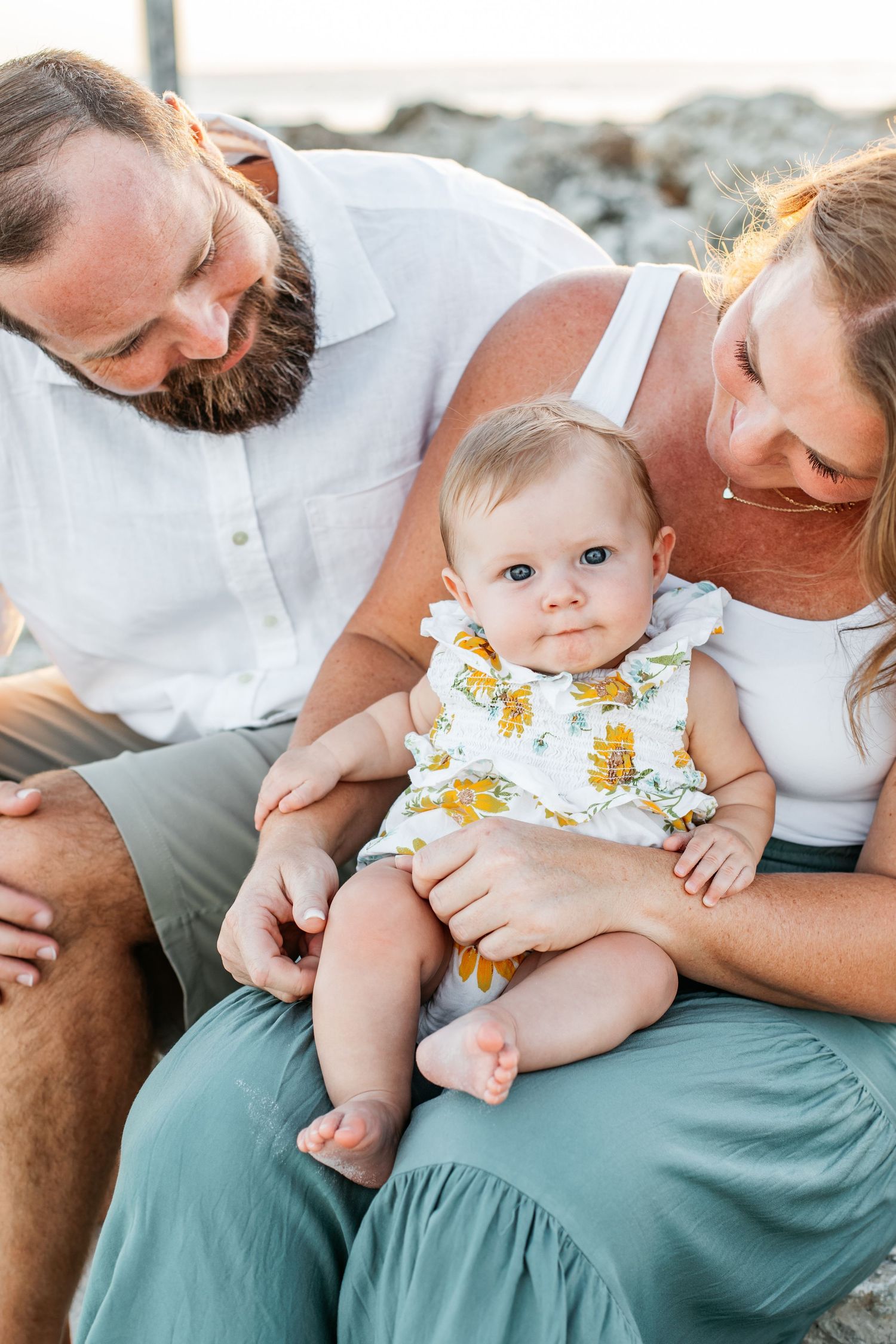 Intimate family moment captured with baby in floral outfit during beach photoshoot.