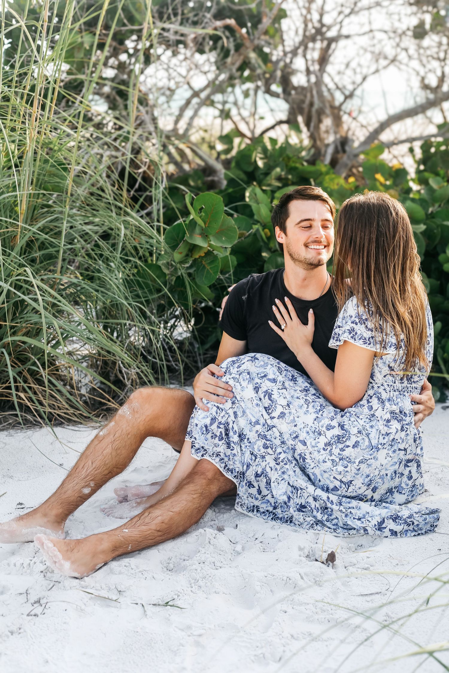 Couple lying on white sand beach surrounded by sea grass and palms.
