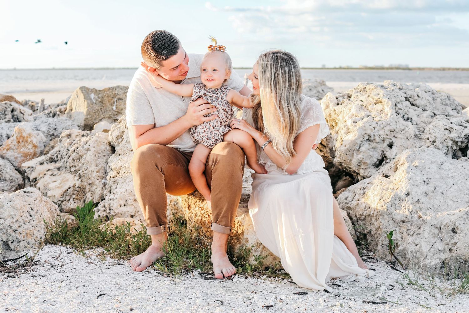A family sits together on coastal rocks during a beachside photo session at sunset.