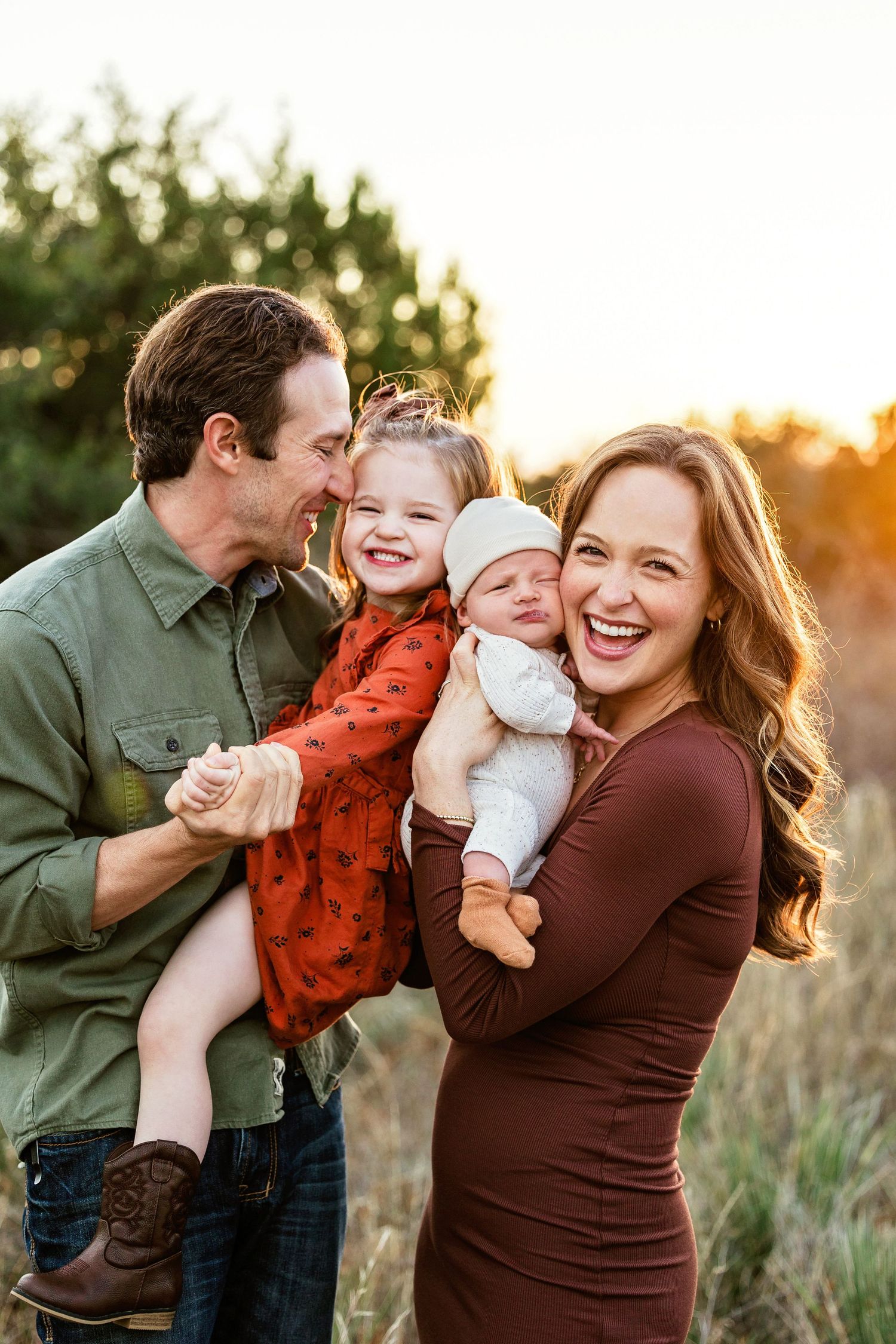 A loving family shares joyful moments together during a golden hour photoshoot in a grassy field.
