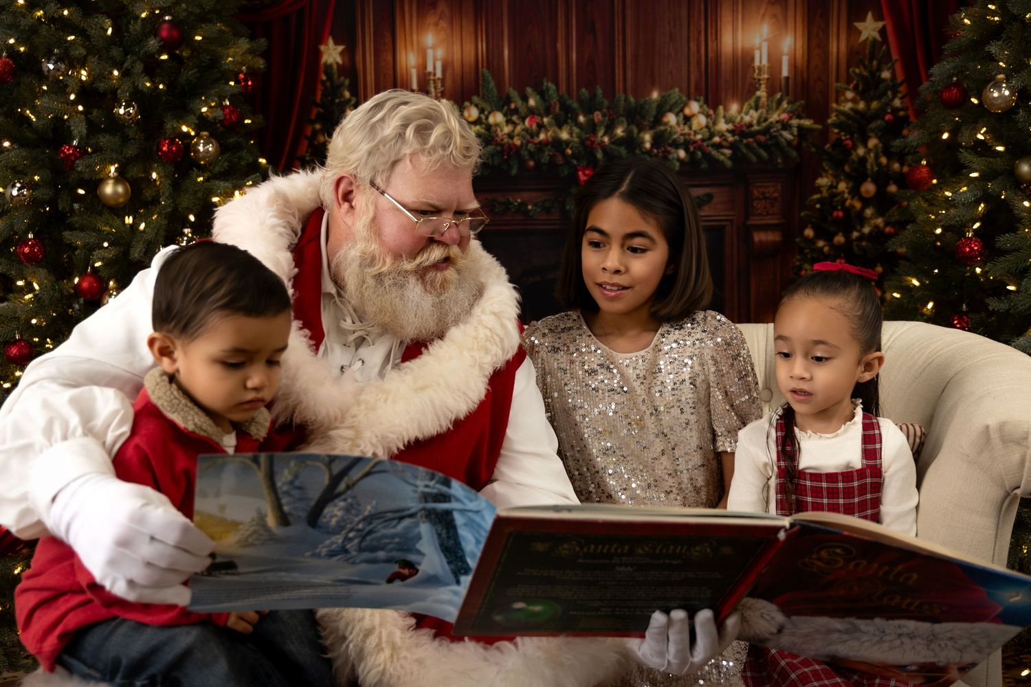 Santa Claus reads a Christmas storybook with three children by a decorated holiday tree.