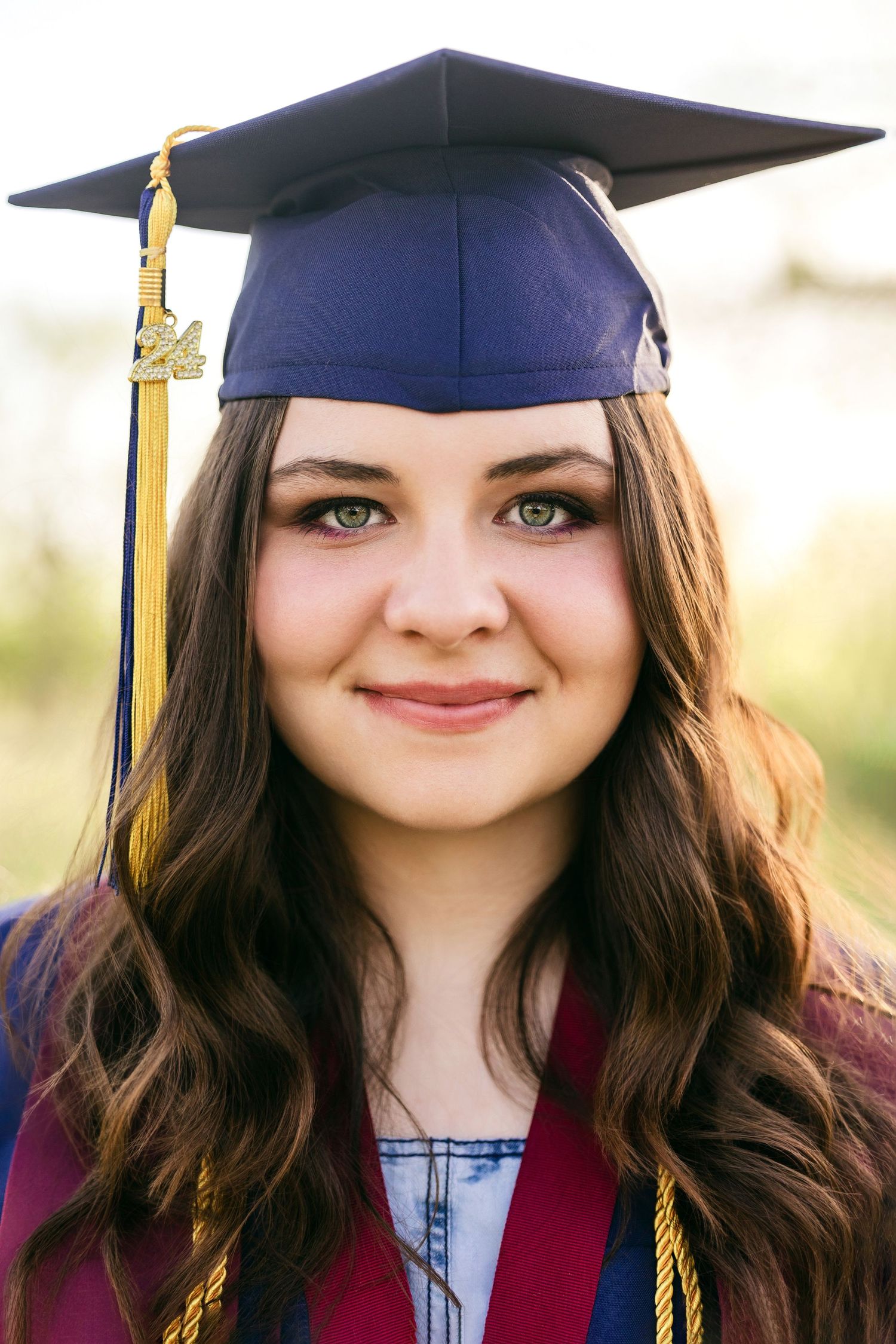 Graduate in cap and gown with burgundy stole smiles in outdoor portrait series at sunset.