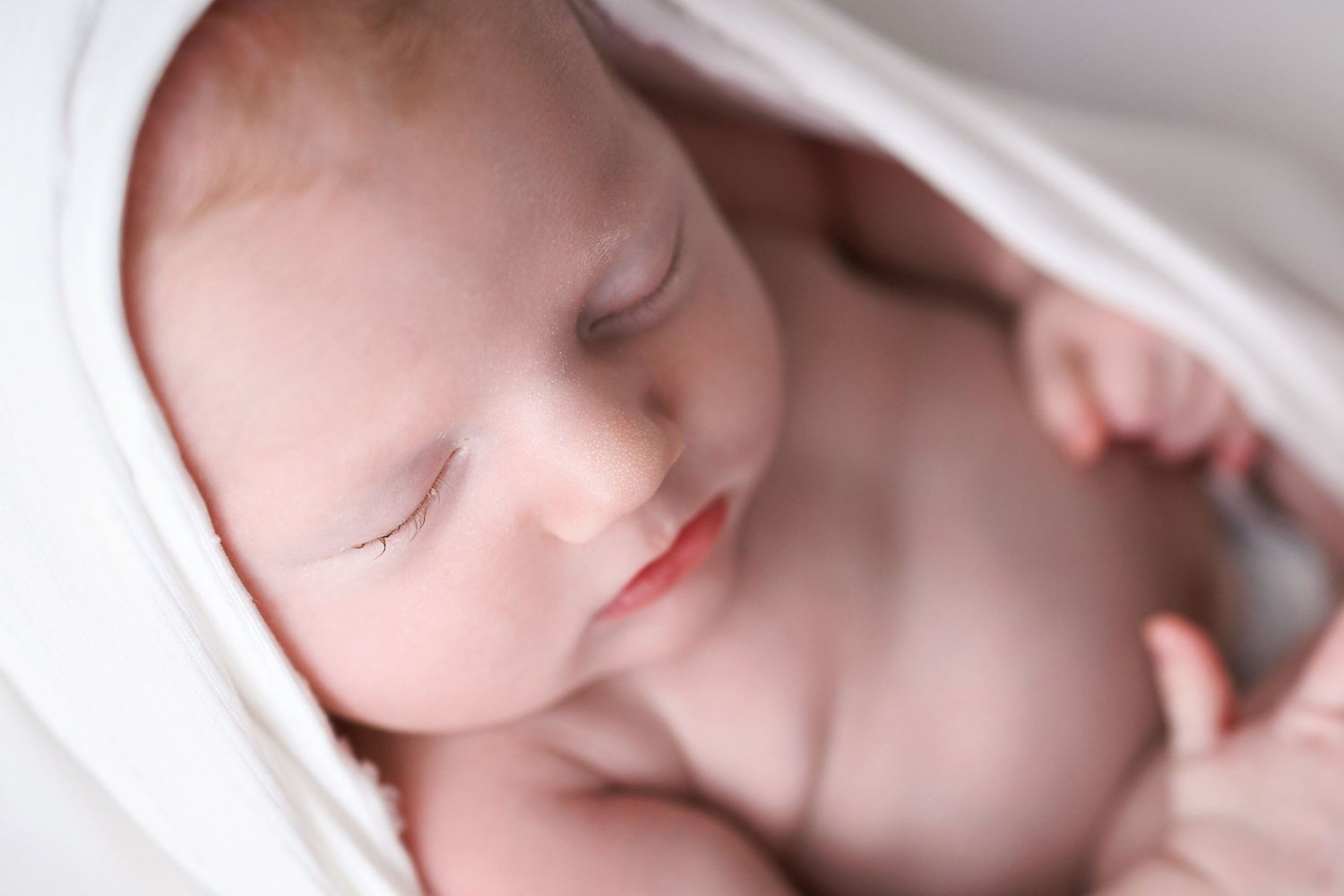 A peaceful sleeping infant wrapped in soft white fabric, shot in gentle natural light.