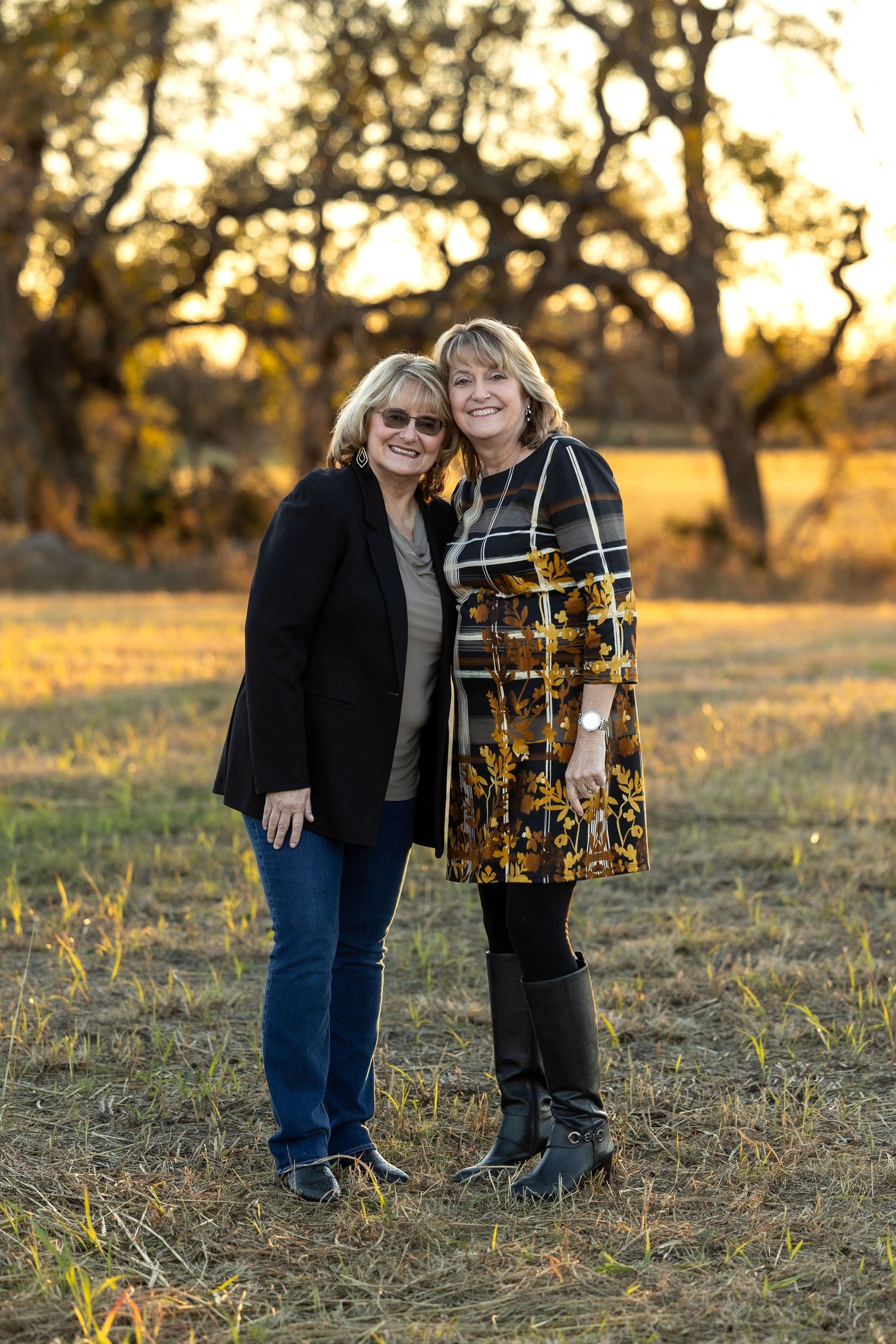 Two people stand together in a grassy field at sunset holding a golden drum or musical instrument.
