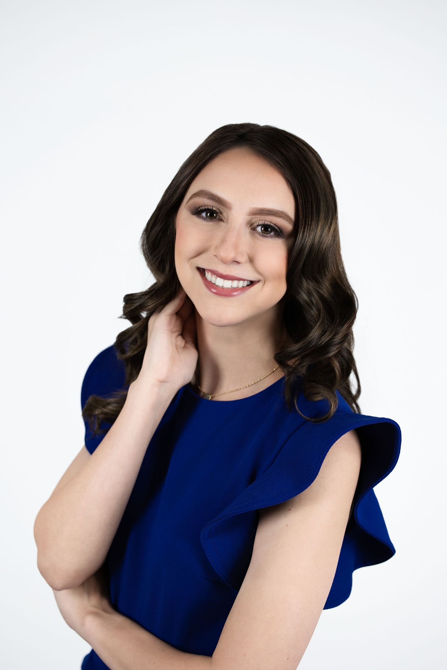 Professional portrait of someone in a royal blue top with ruffled sleeves posing against a white background.