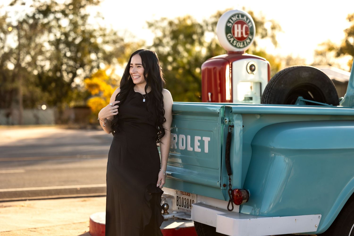 A vintage turquoise Chevrolet pickup truck is parked near a retro gas pump during golden hour.